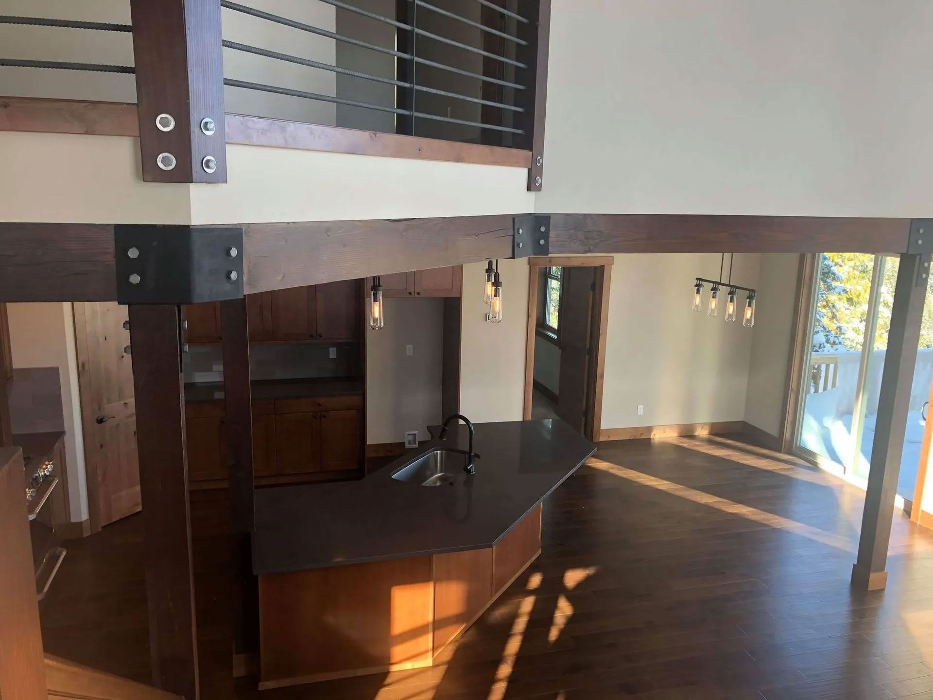 Interior view of a modern home with a kitchen island, dark wood floors, and a loft with a metal railing.