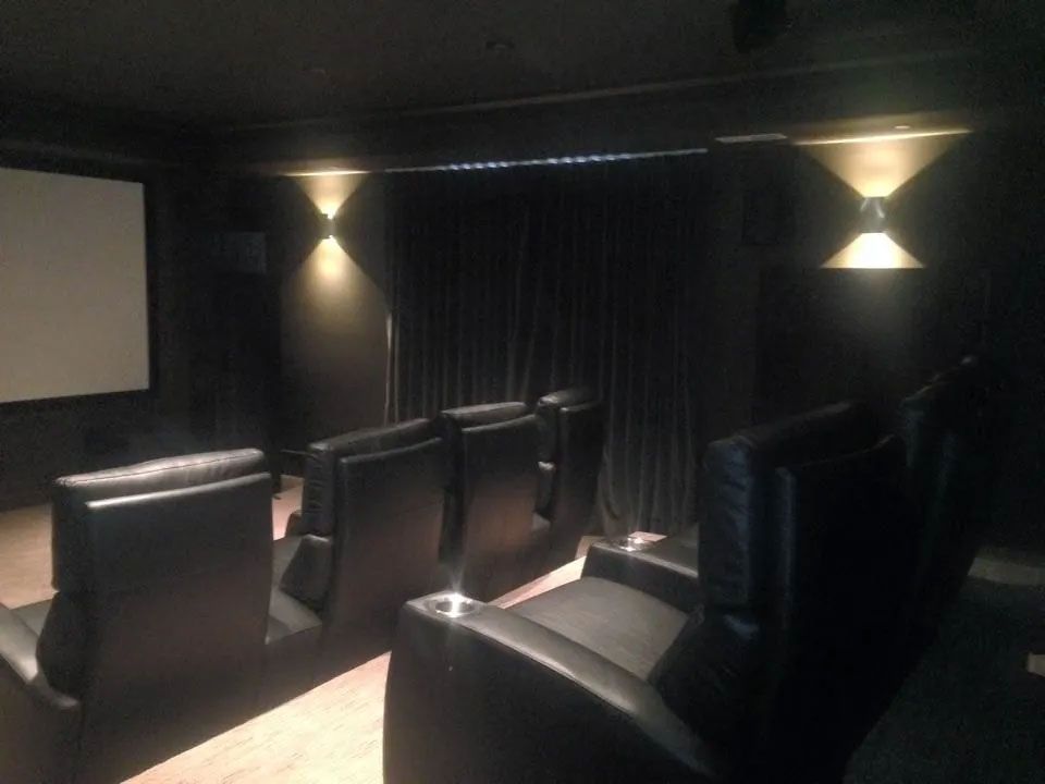 Home theater with black leather recliners, a screen, and sconce lighting against black walls.