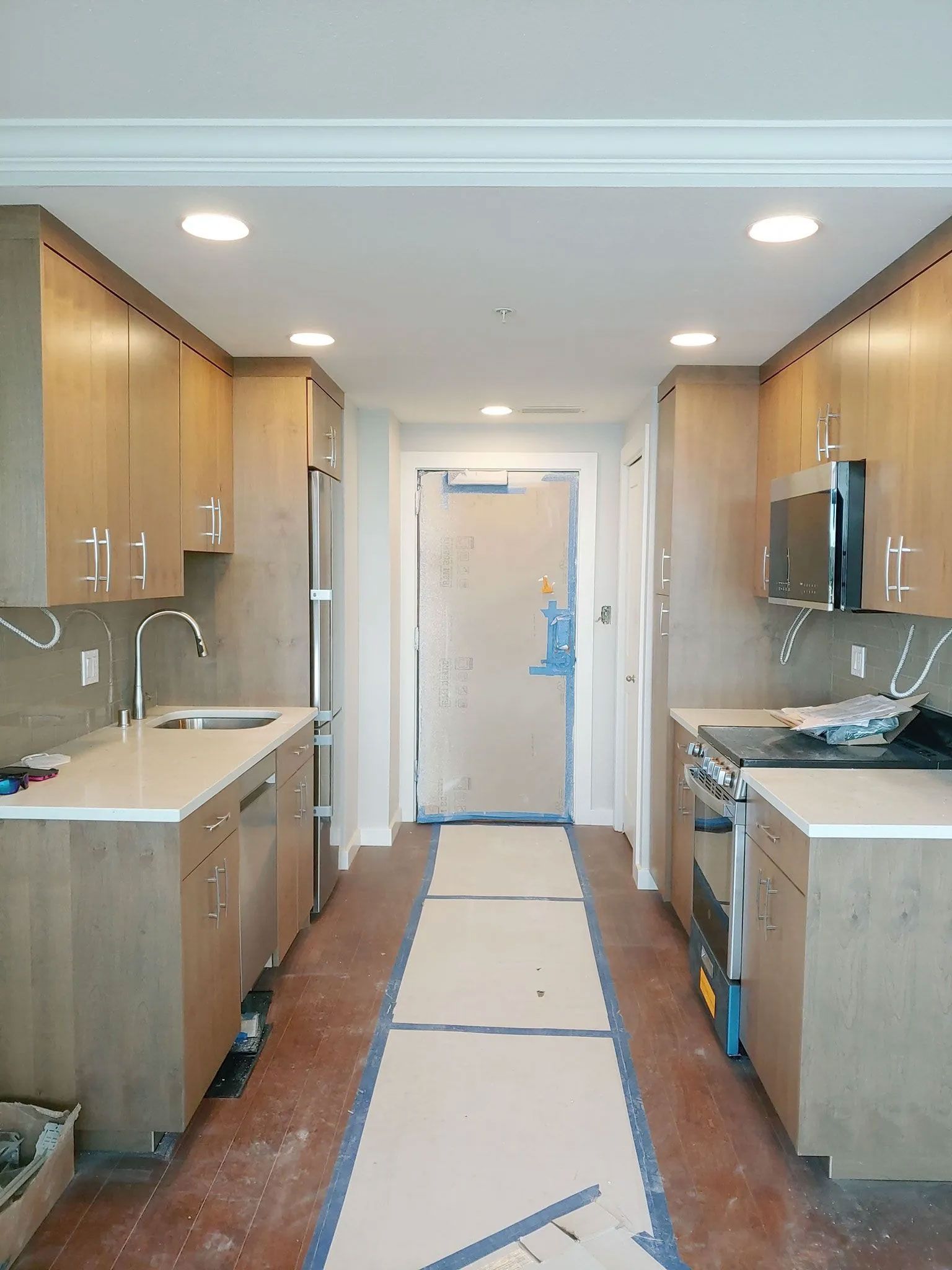 Narrow kitchen with light wood cabinets, white countertops, and a door at the end.
