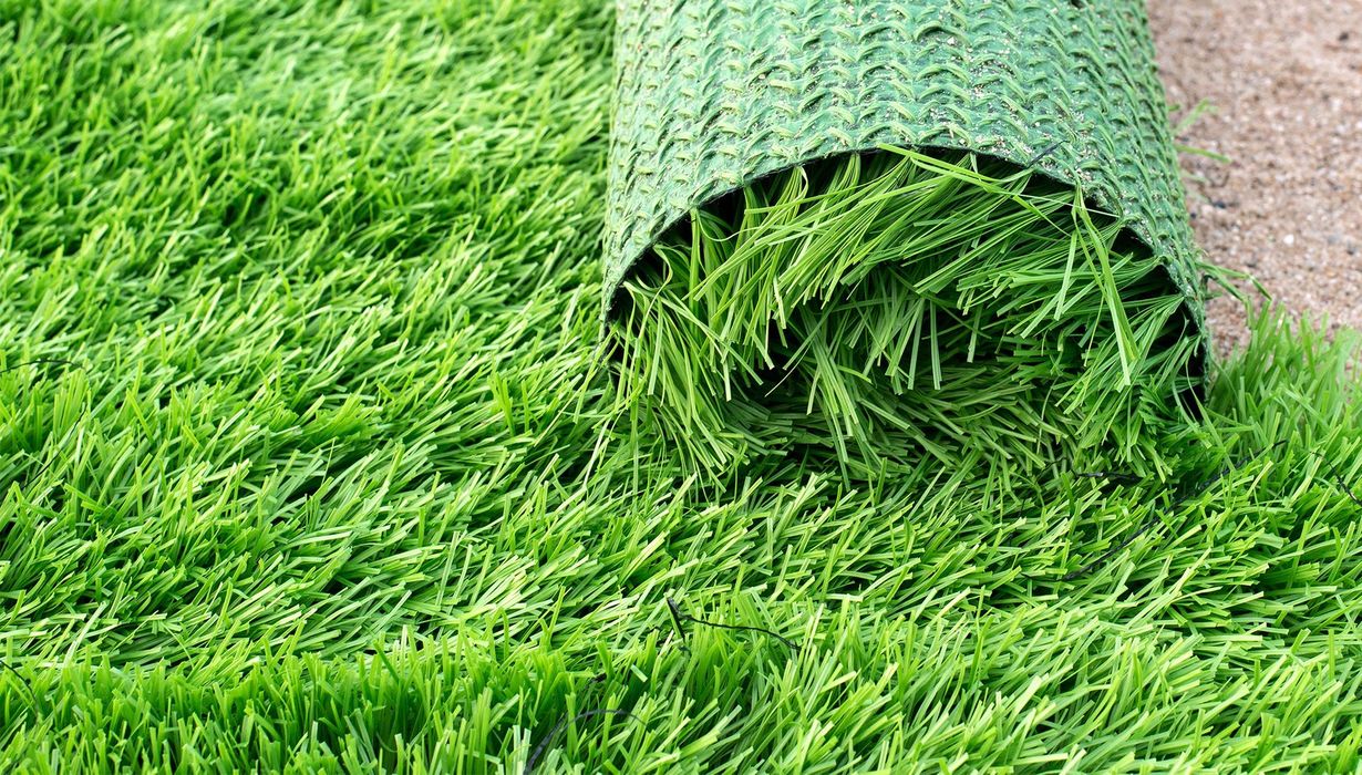 Roll of bright green artificial turf partially unrolled on sand.