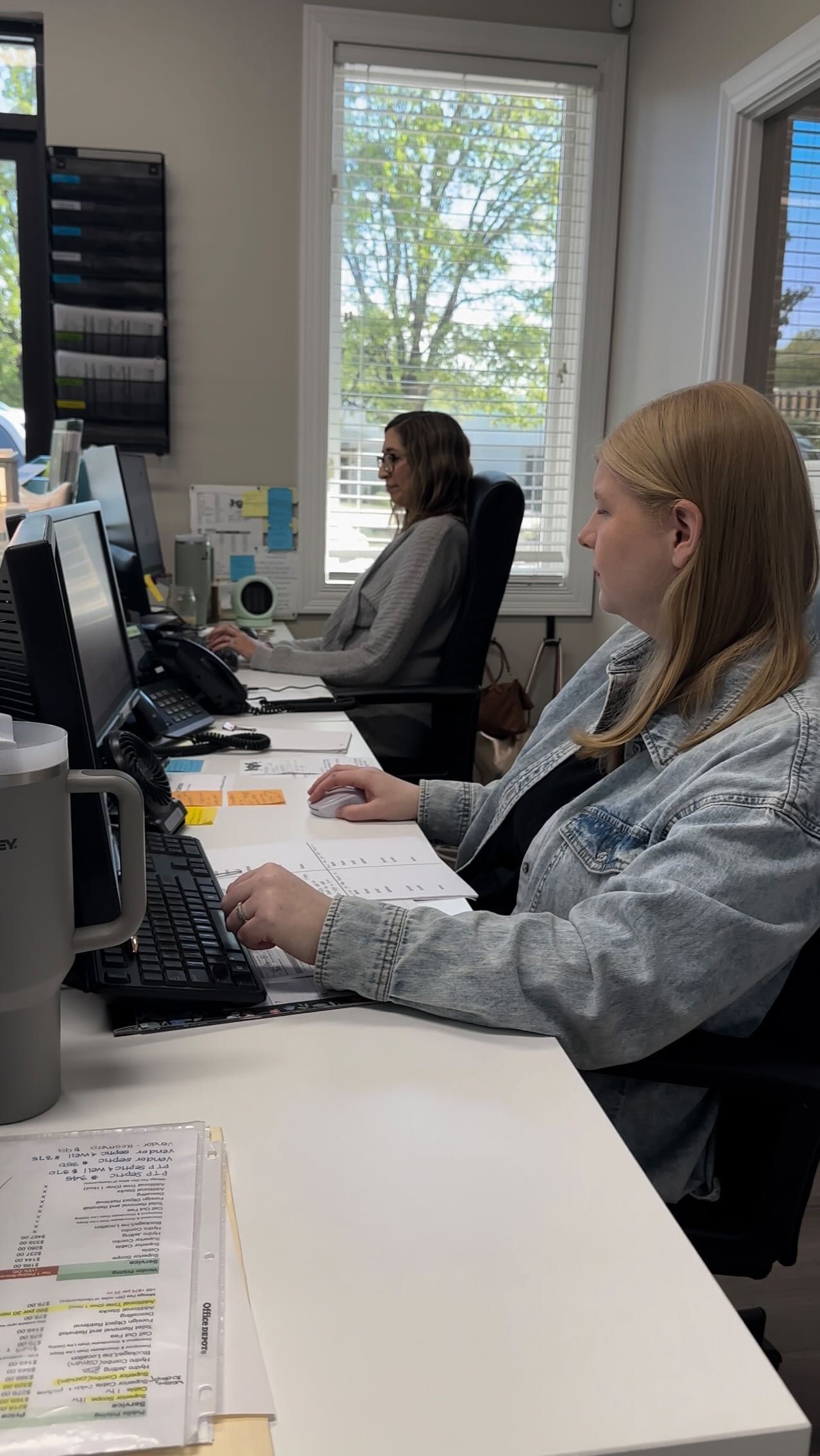Two women are sitting at desks in an office working on computers.