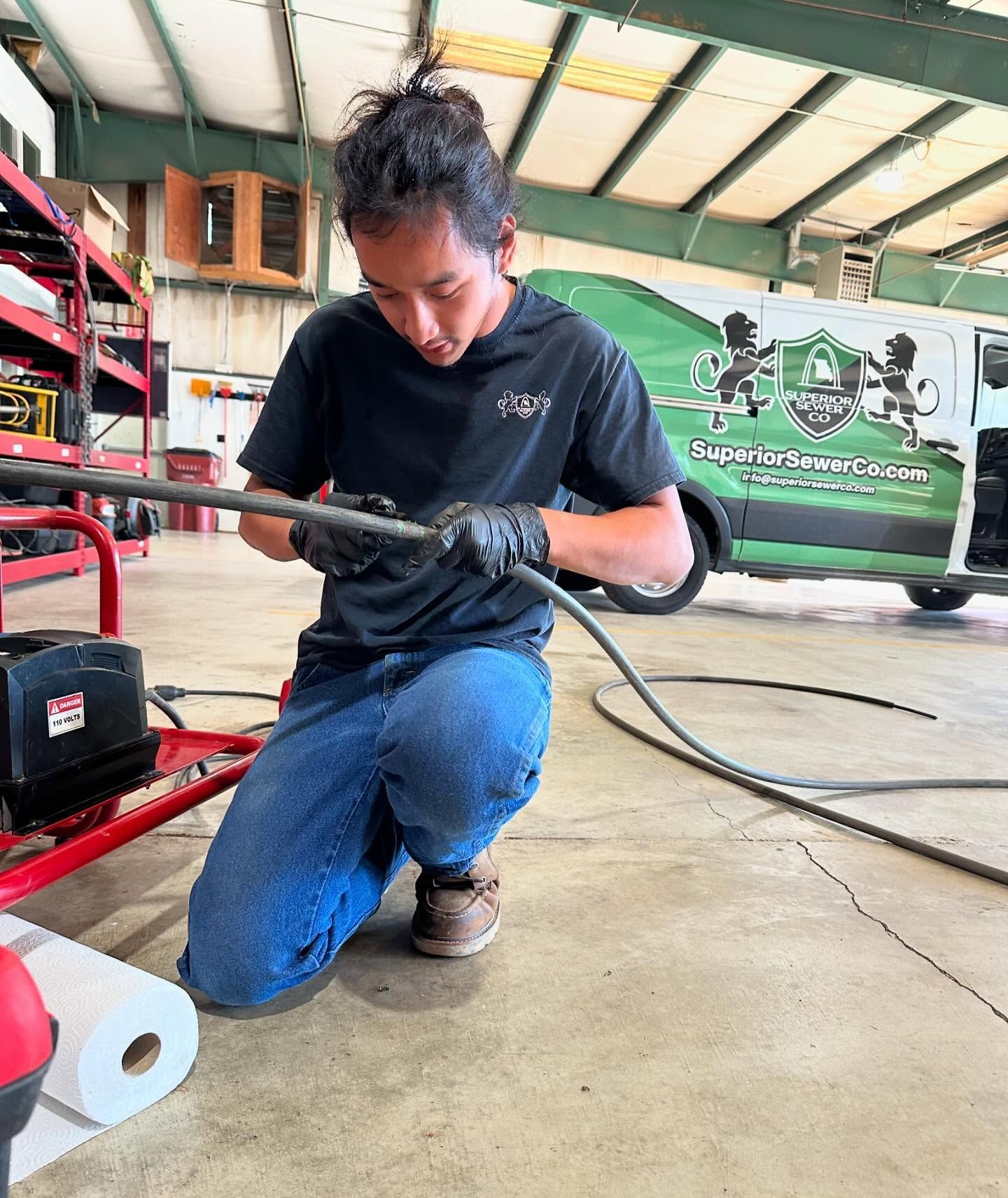 A man is kneeling down in a garage holding a hose.