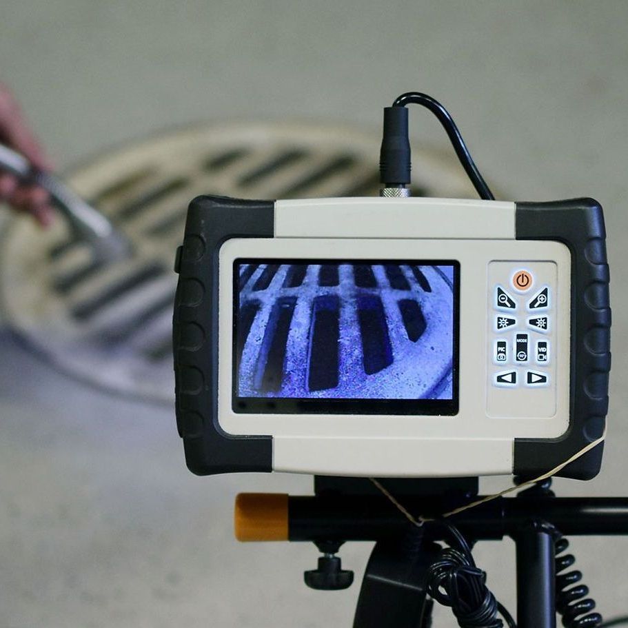 A manhole cover is being examined by a camera on a tripod.