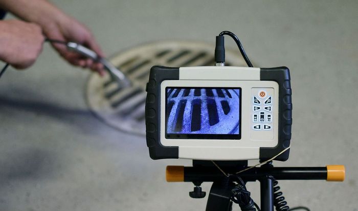 A manhole cover is being examined by a camera on a tripod.