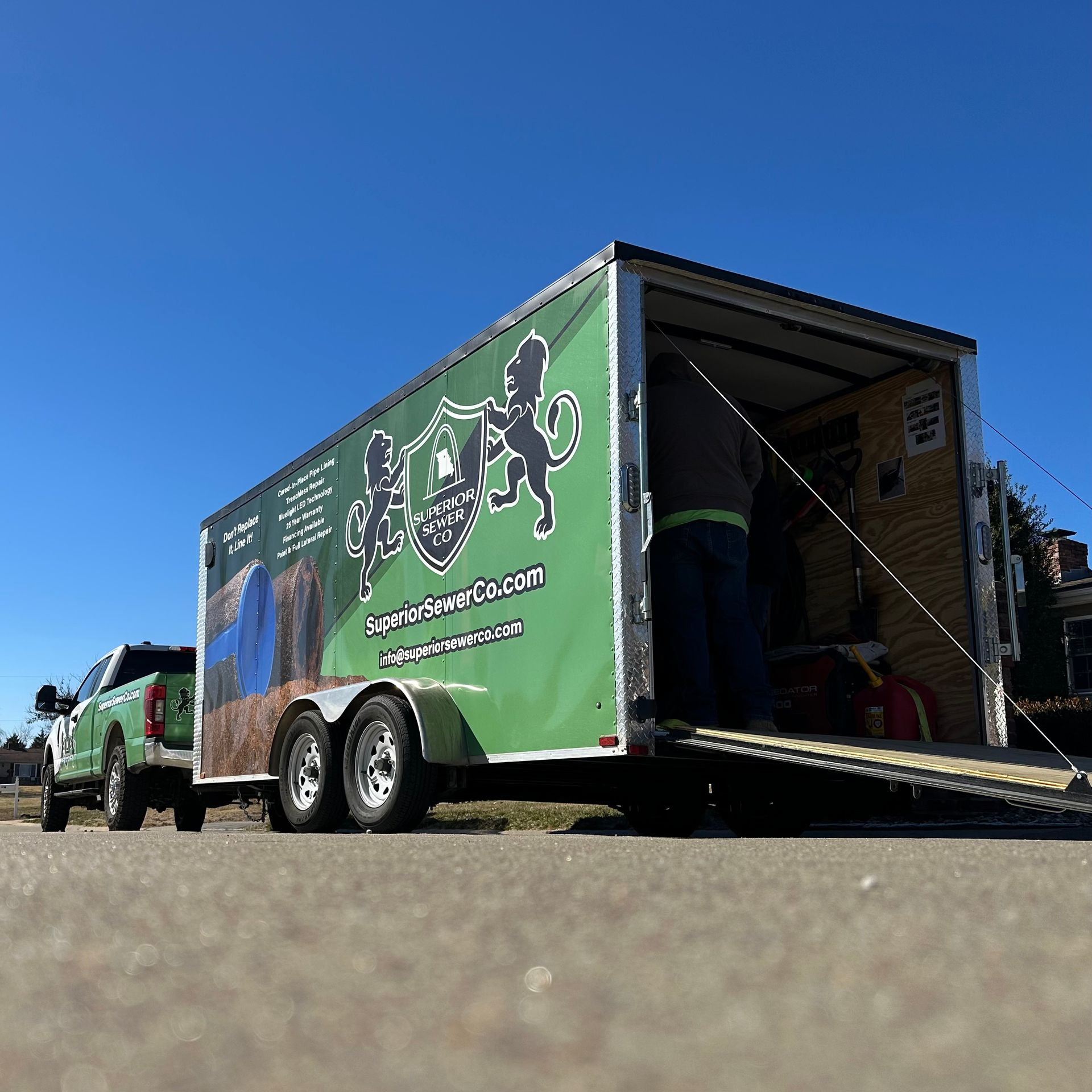 A green truck is pulling a green trailer on a road.