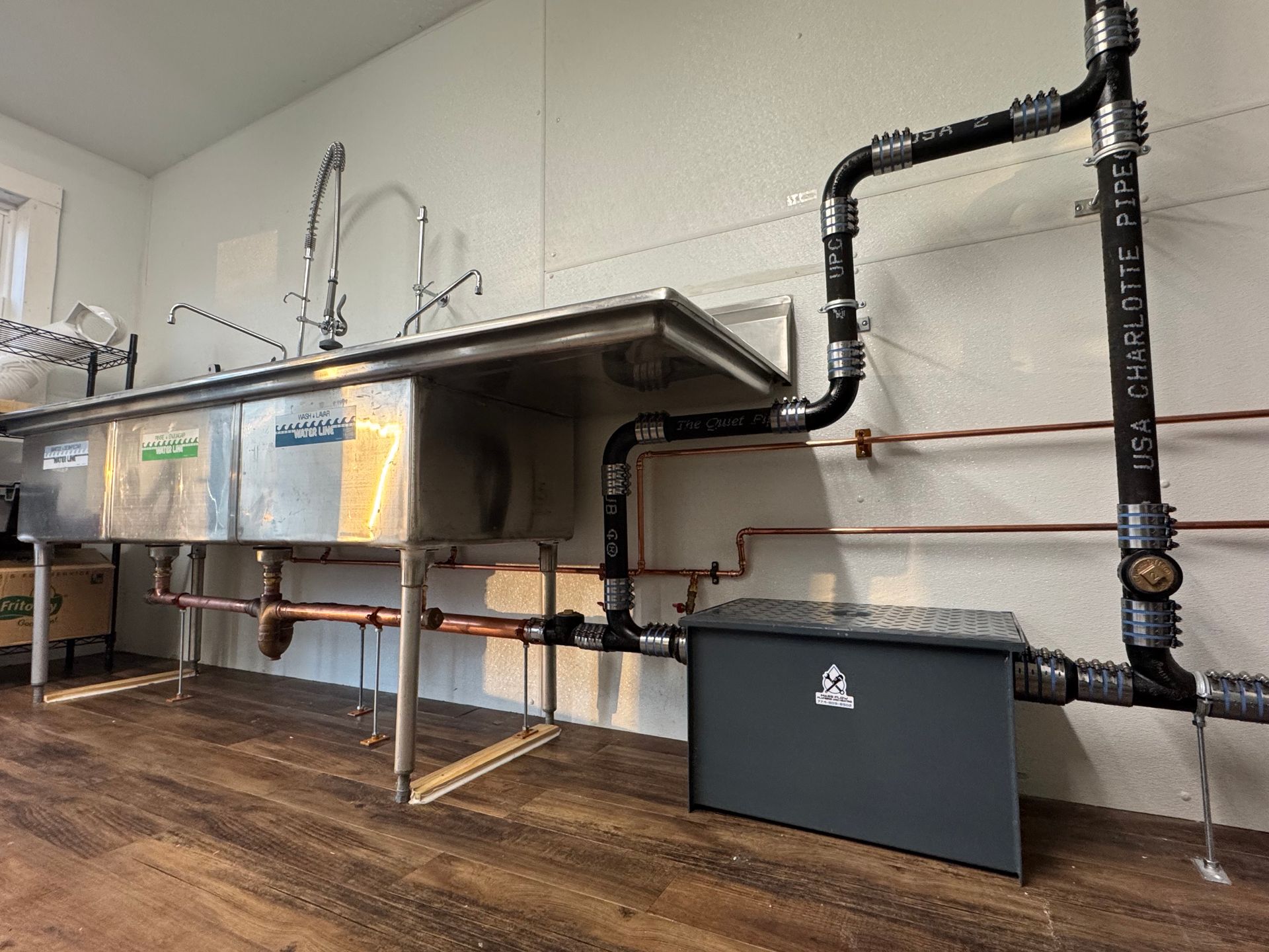 A kitchen with stainless steel sinks and copper pipes