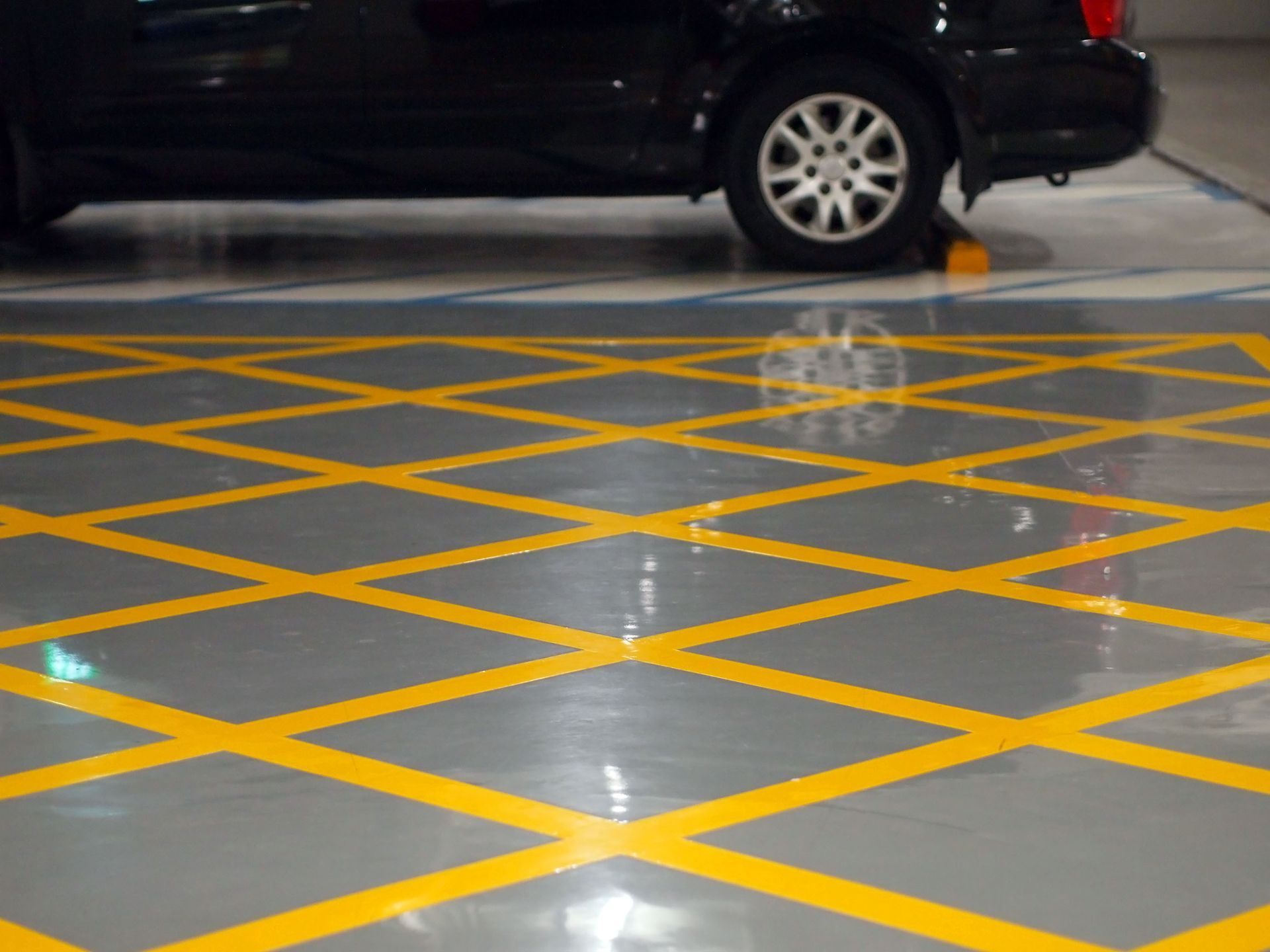Black car parked in space with yellow crosshatch markings on a gray floor.