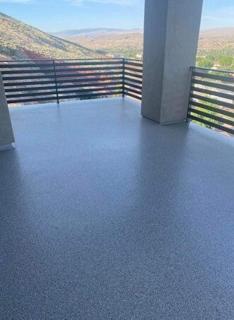 A gray, epoxy-coated outdoor patio with horizontal wooden railings, overlooking a mountain landscape.