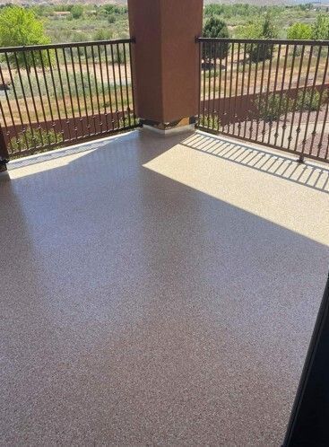 A balcony with a brown and tan speckled floor and a metal railing overlooks a scenic landscape.