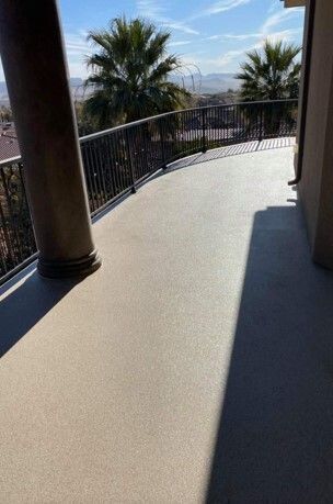Balcony with tan flooring, black railing, palm trees, and mountain view under a partly cloudy sky.