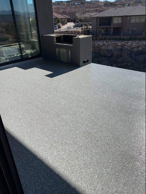 Gray speckled concrete patio with built-in outdoor kitchen, view of distant houses and hills.