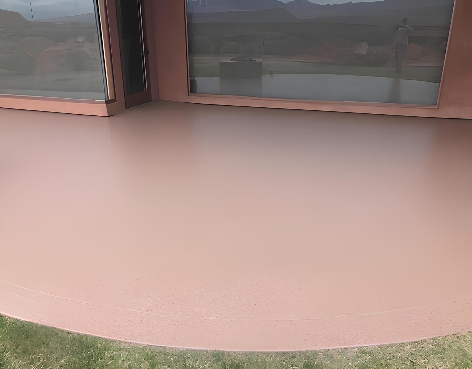 A smooth, rose-colored concrete patio with large windows in the background and a grassy lawn.