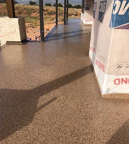 Brown speckled epoxy coated patio floor. Construction materials in the corner; building under construction in a desert setting.