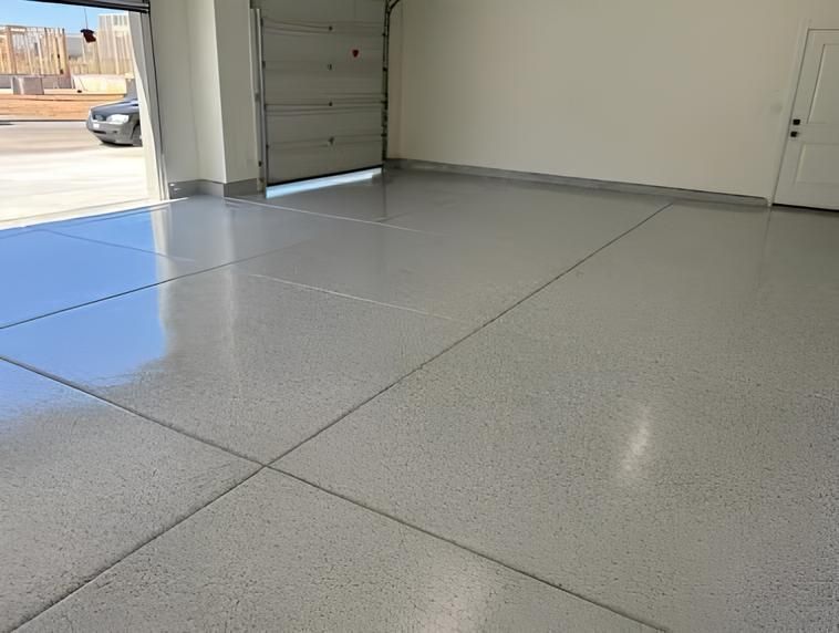 A garage interior with a shiny, light gray epoxy floor. The garage door is open, and a car is visible outside.