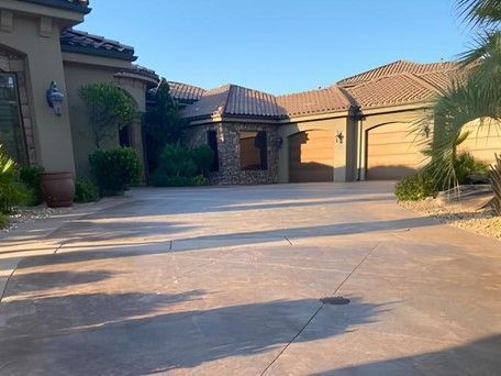 Driveway leading to a large house with a tile roof and two garage doors; sunny outdoor setting.