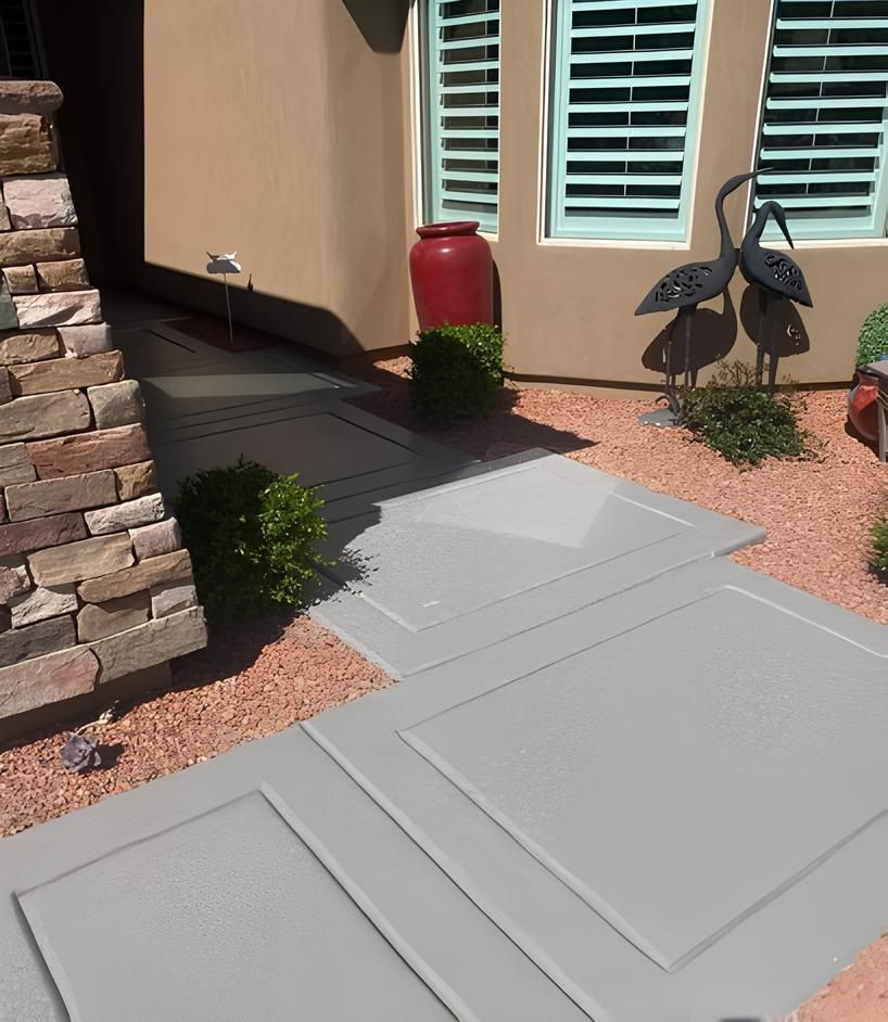Gray concrete pathway leading to a doorway, flanked by landscaping and decorative metal birds.
