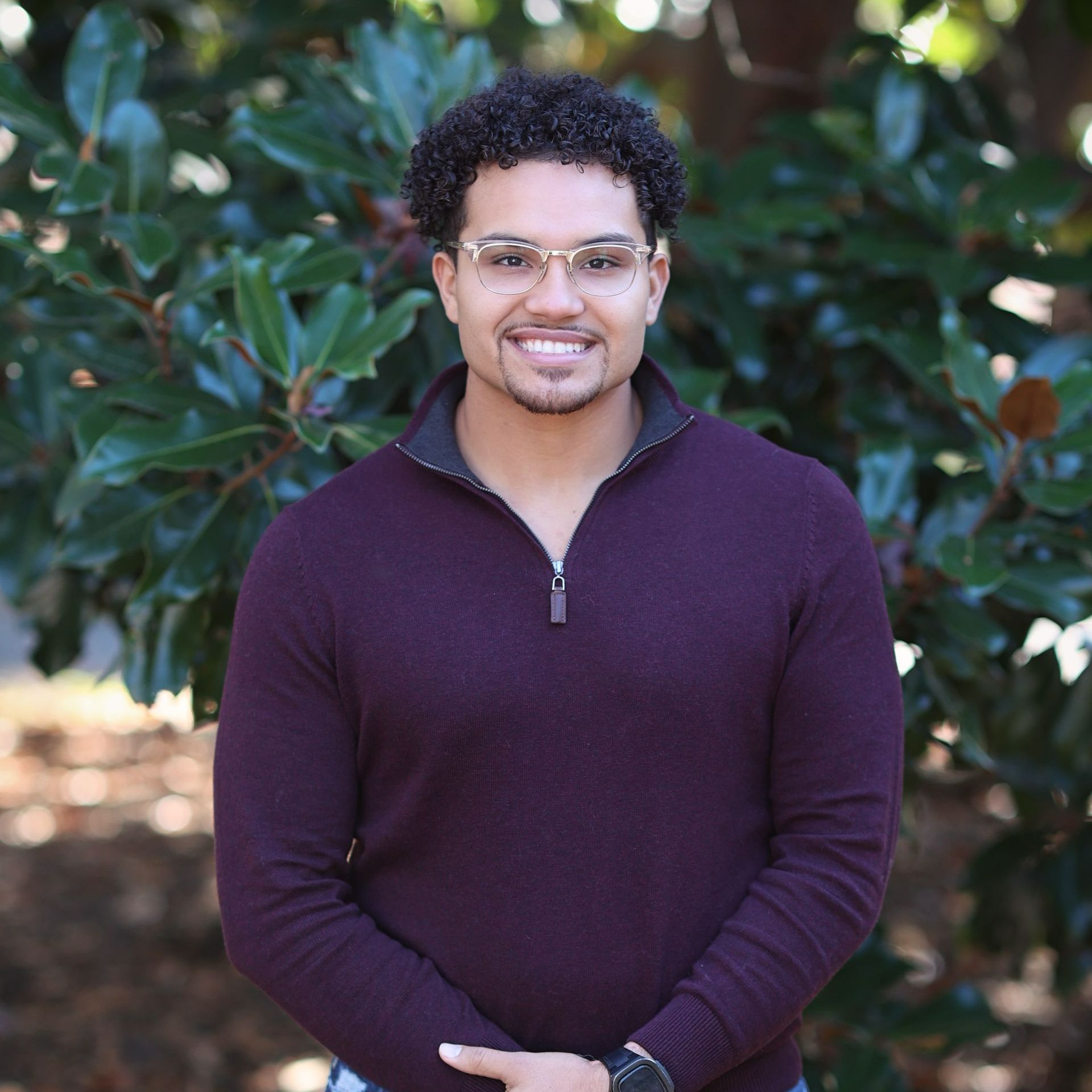 a man wearing glasses and a purple sweater is standing in front of a tree