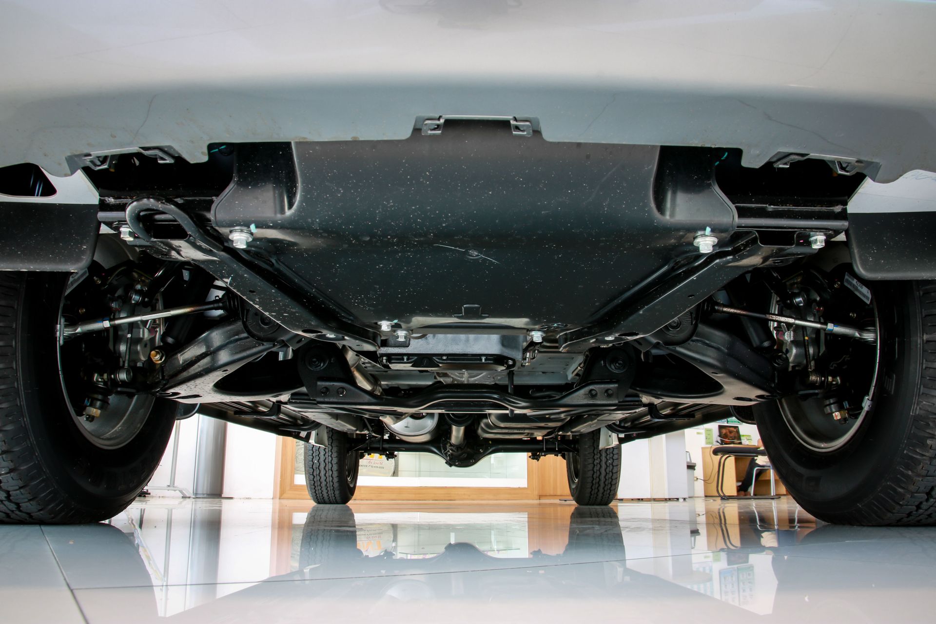 Underside of a black vehicle, showing suspension, wheels, and protective undercarriage panels, set indoors on a shiny floor.