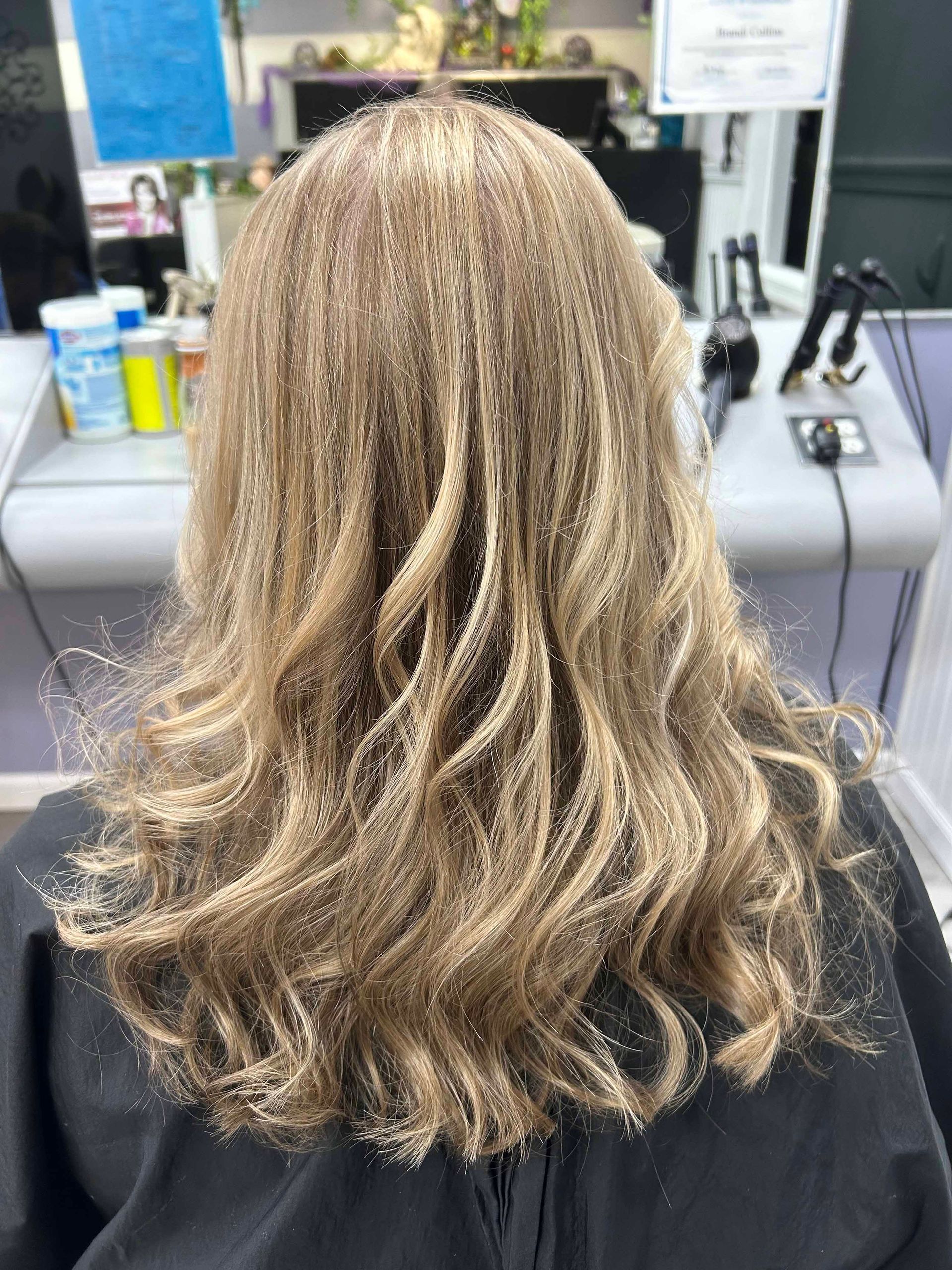 A woman with long blonde hair is sitting in a chair in a salon.