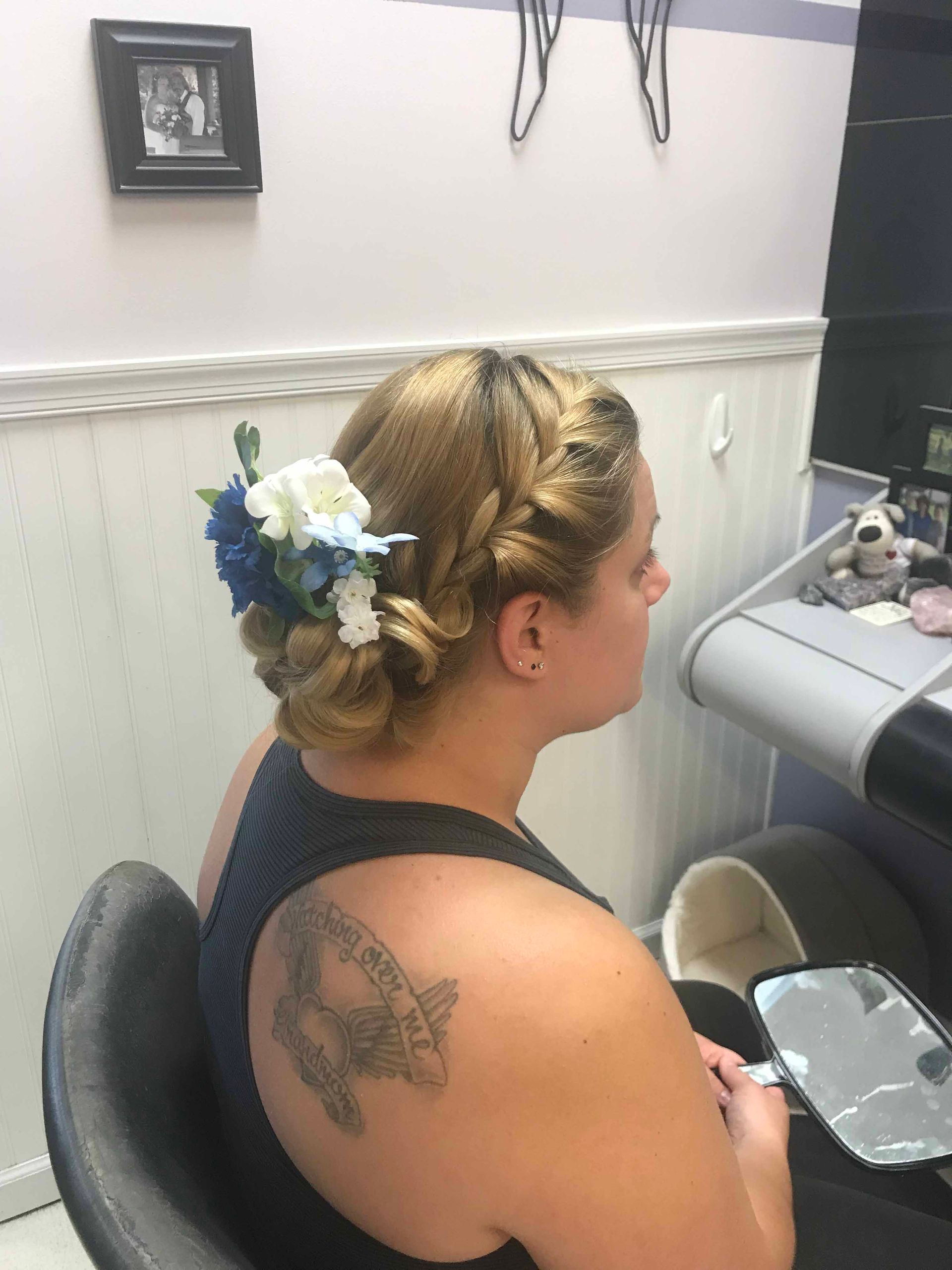 A woman with a tattoo on her back is sitting in a chair with flowers in her hair.