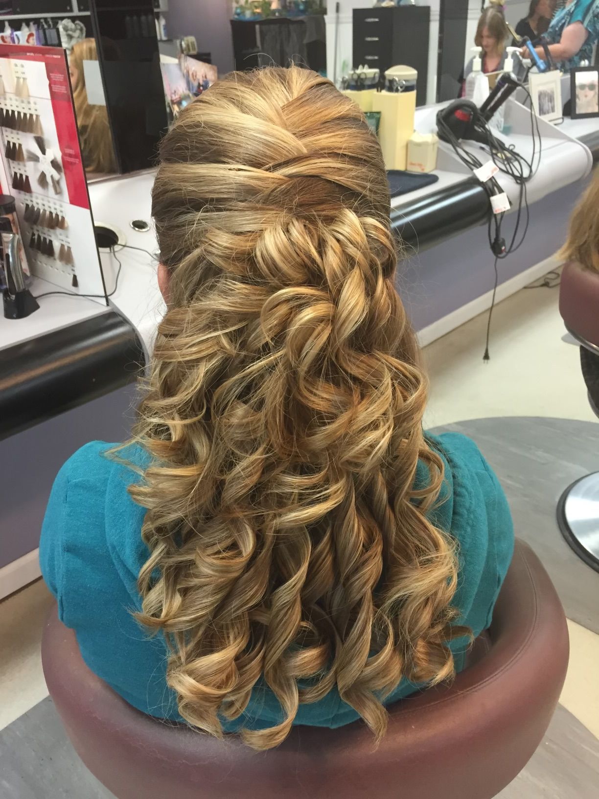 A woman is sitting in a chair with her hair in a half up half down hairstyle.