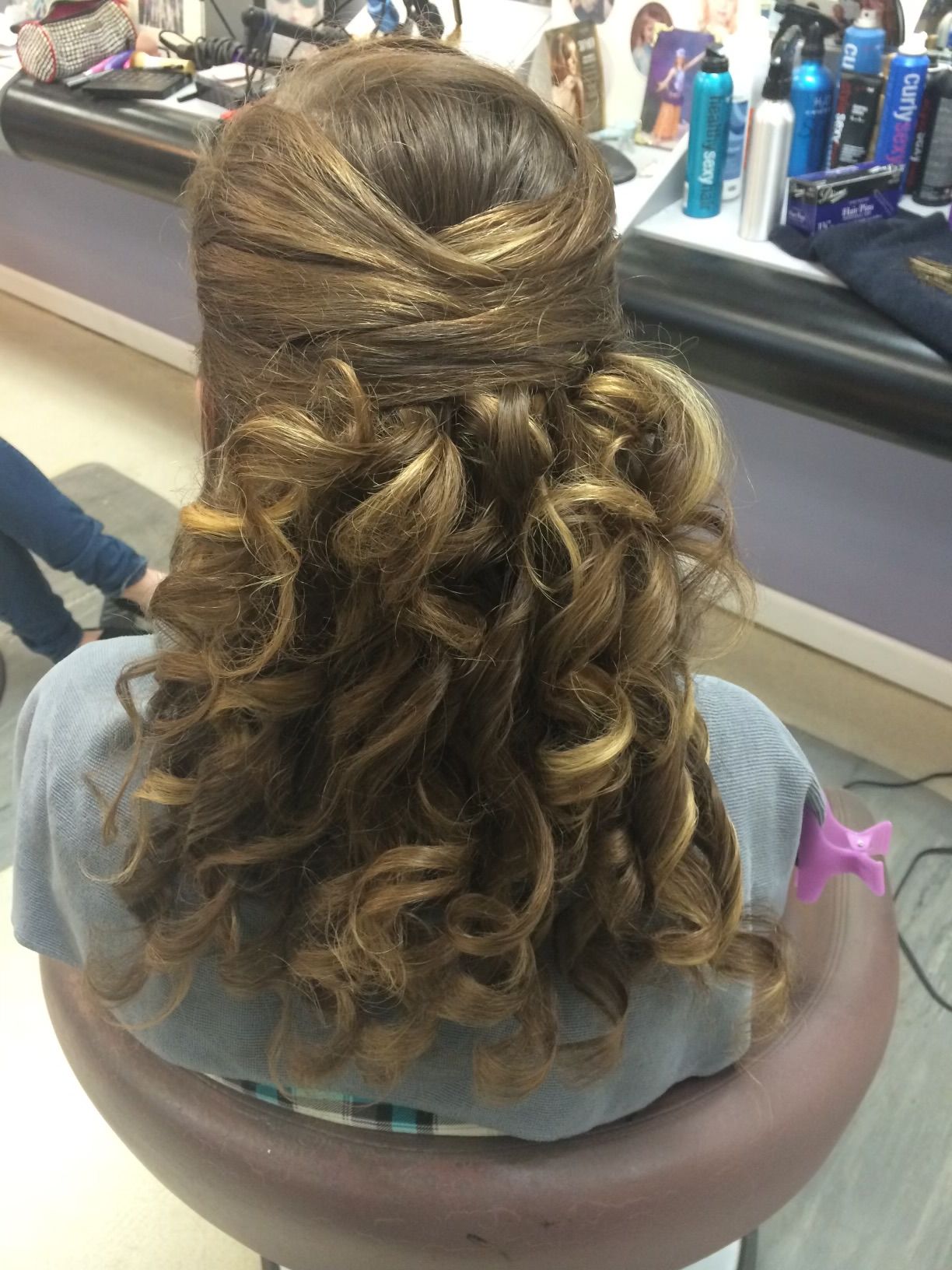A woman is sitting in a chair with her hair in a half up half down hairstyle.