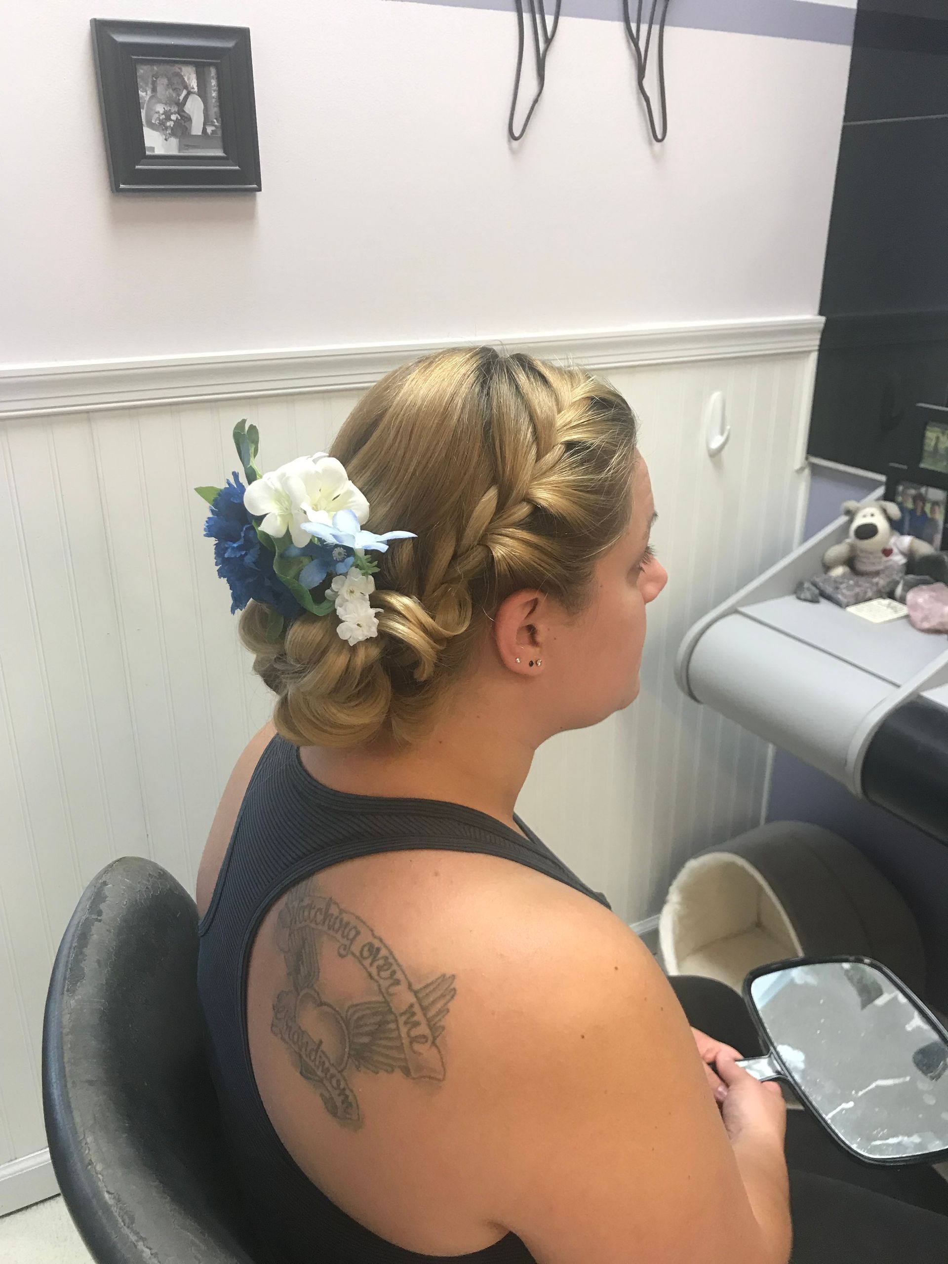 A woman with a tattoo on her back is sitting in a chair with flowers in her hair.