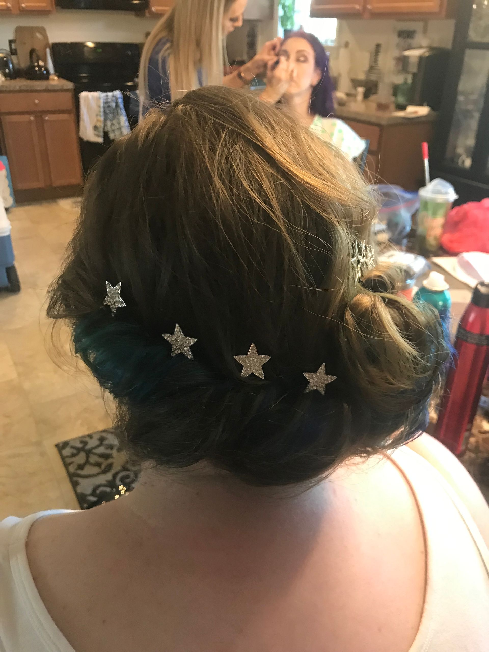 A woman is getting her hair done in a kitchen.