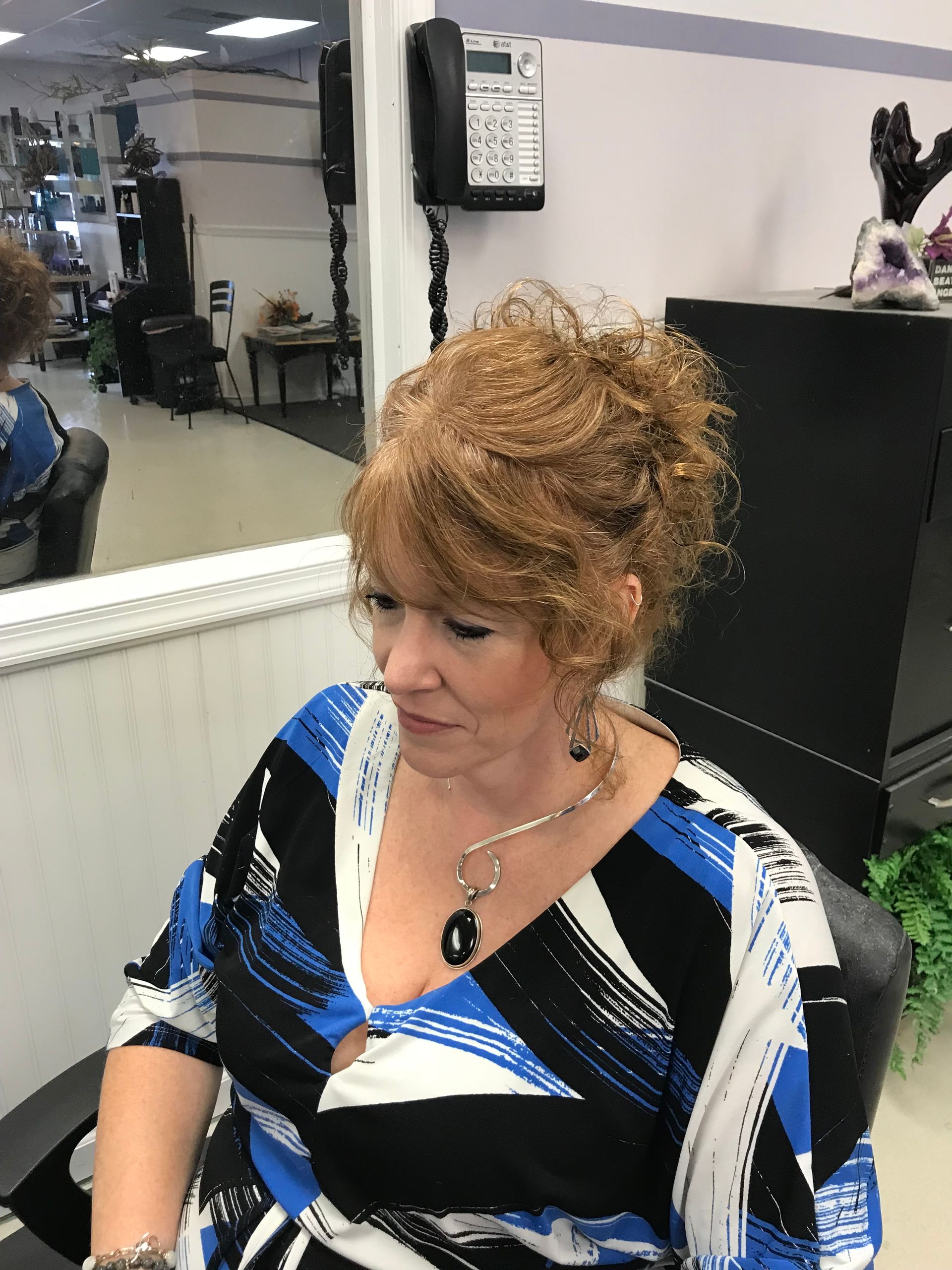 A woman in a blue and white dress is sitting in a chair in front of a mirror.