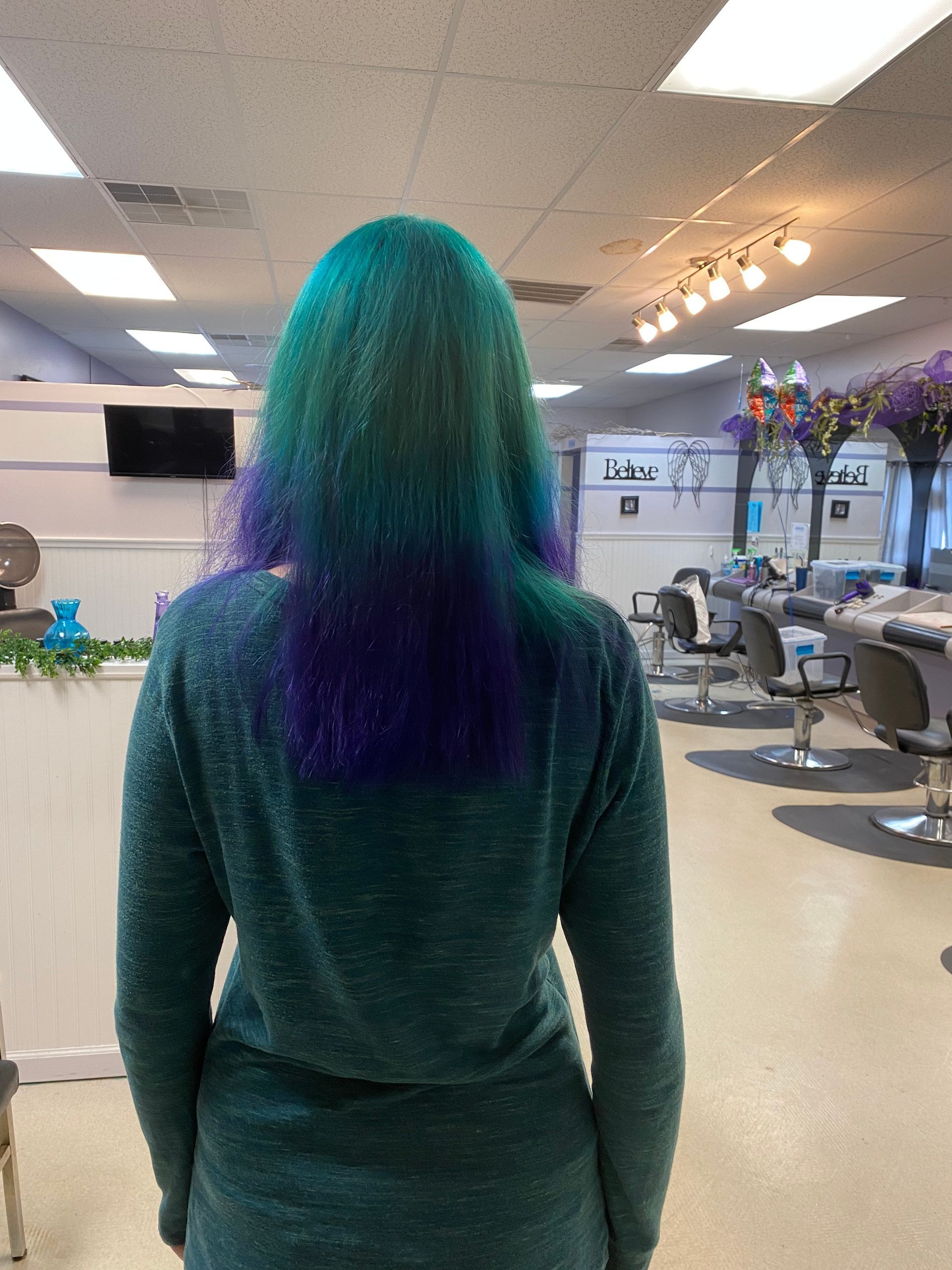 A woman with green and purple hair is standing in a salon.