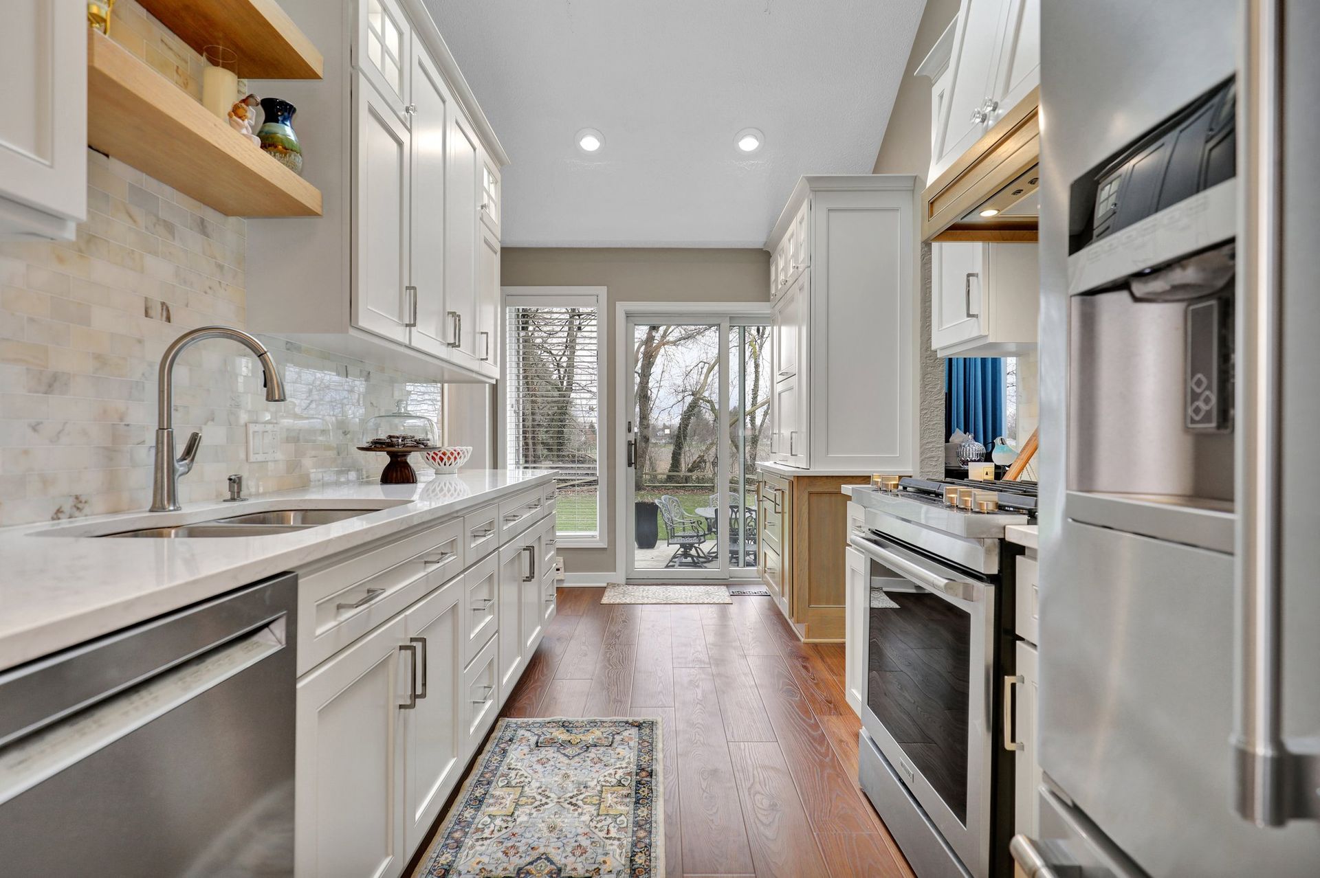 Bright narrow kitchen with white cabinets, stainless steel appliances, wood floor, and glass doors at the end