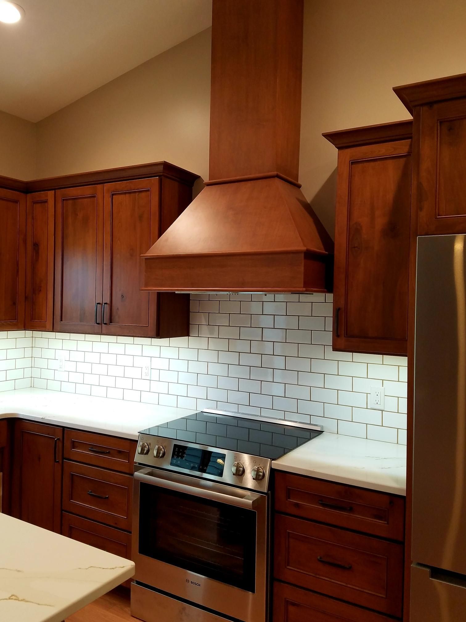 Modern kitchen with dark wood cabinets, copper range hood, white backsplash, and stainless steel stove.