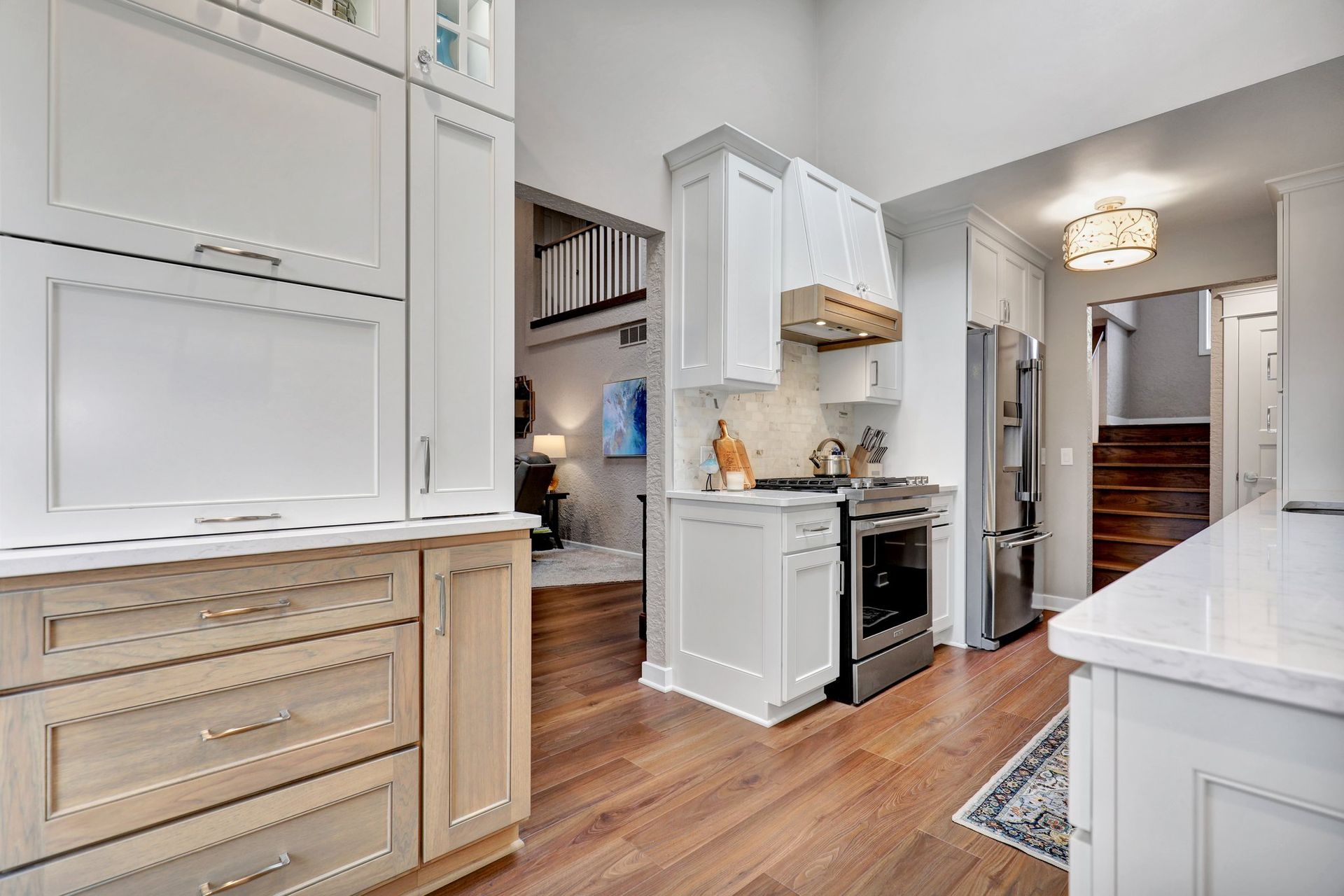 Bright white kitchen with wood floors, island, stove, and staircase in the background