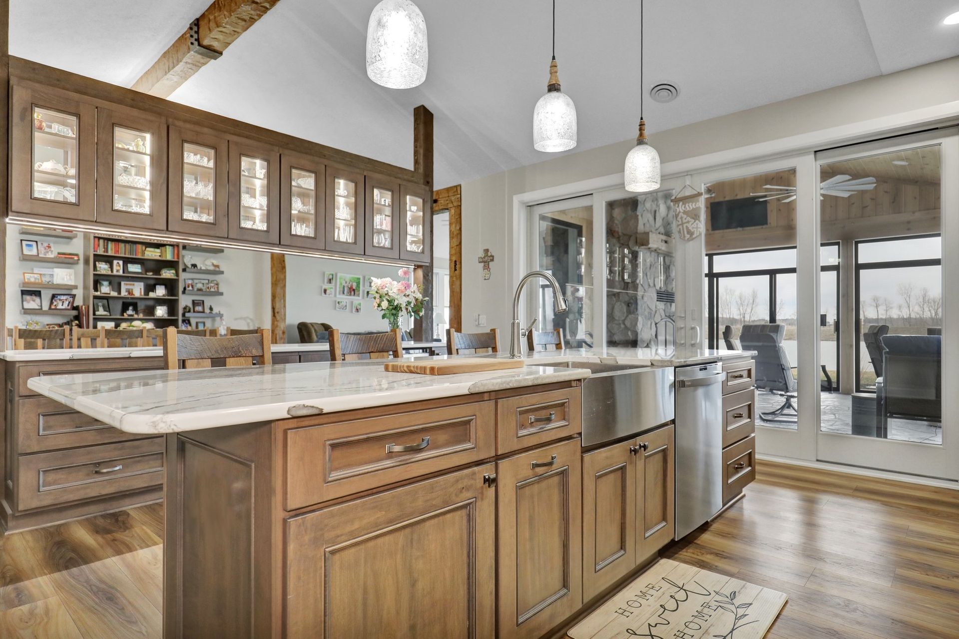 Modern kitchen with large marble island, wood cabinets, pendant lights, and open view to a patio.