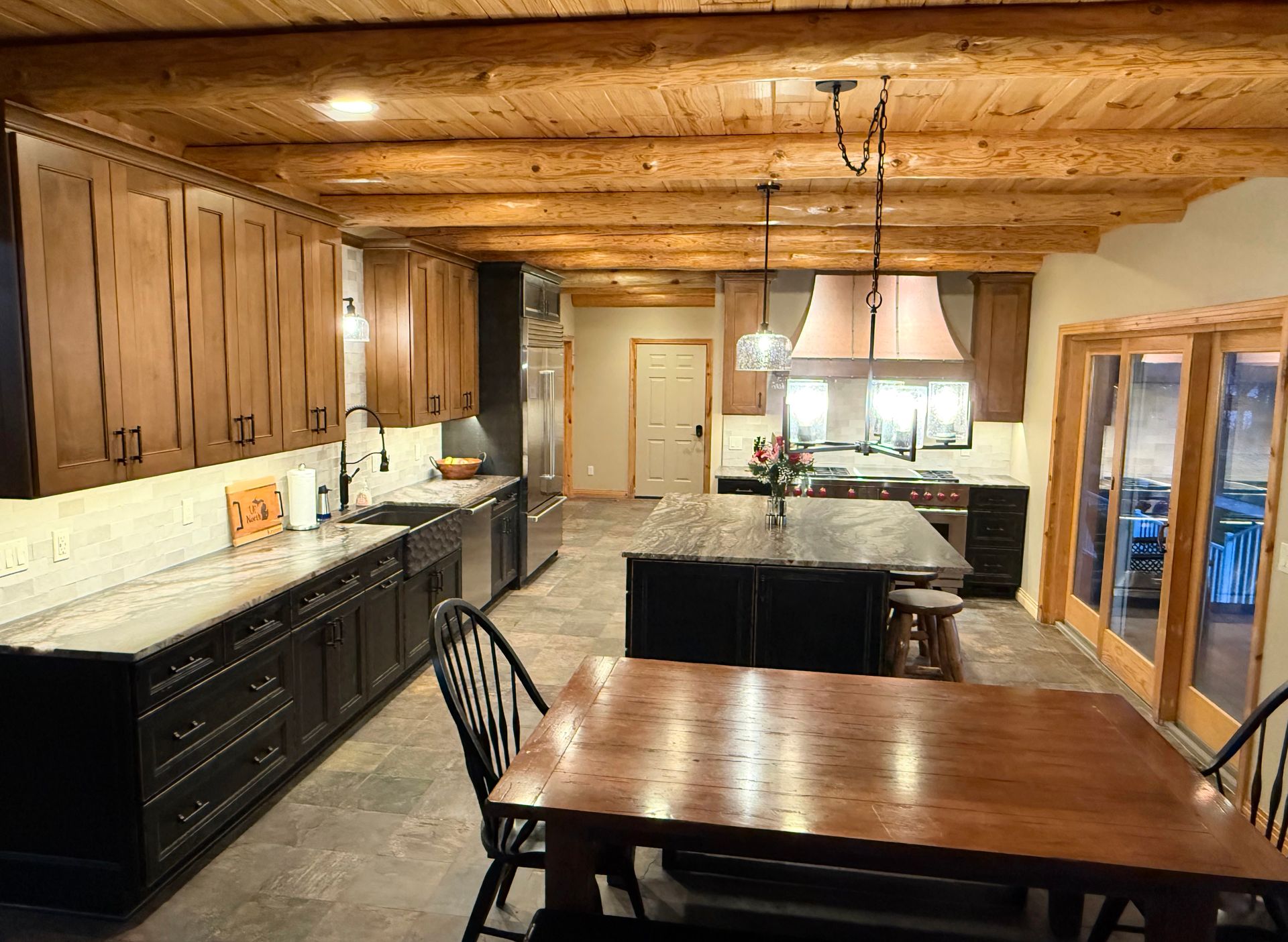 Wood-paneled kitchen with dark cabinets, black island, dining table, and pendant lights