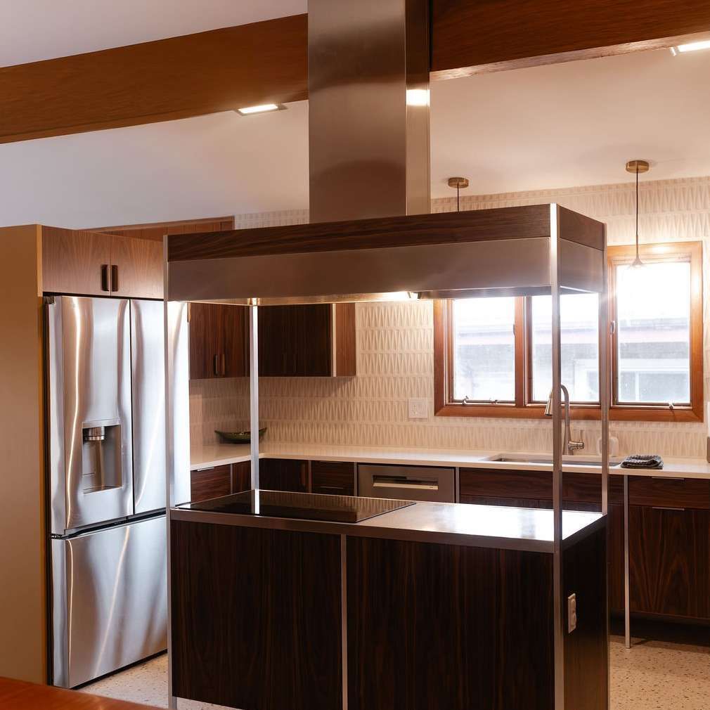 Modern kitchen with stainless steel refrigerator, dark wood cabinets, and a central island under warm lighting