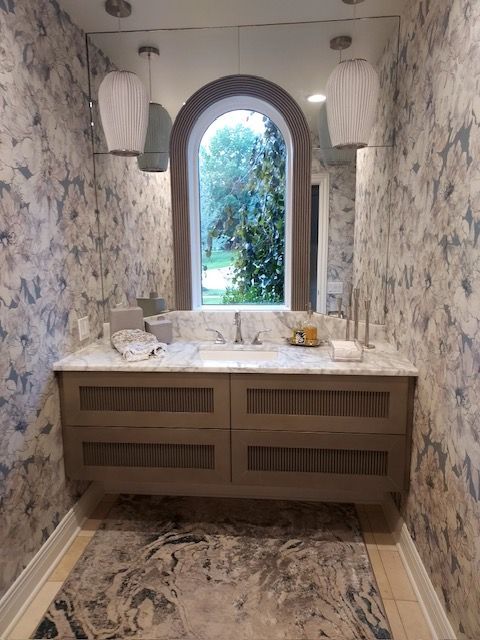 Narrow floral bathroom with double vanity, round mirror, and arched window overlooking greenery