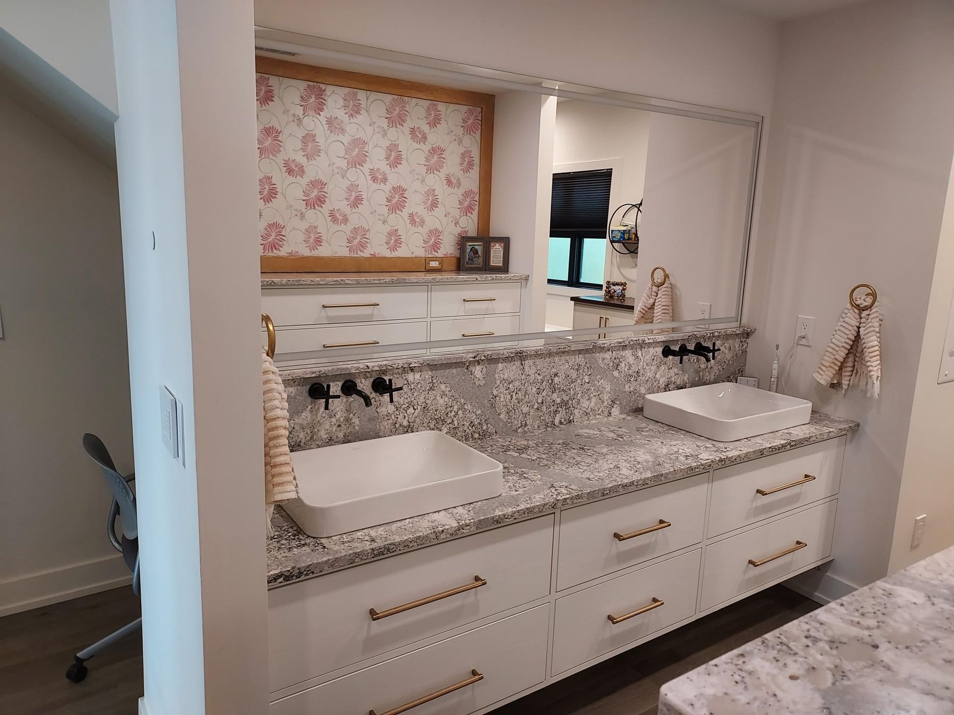 Bright bathroom vanity with twin sinks, marble countertop, and pink floral wallpaper accent.