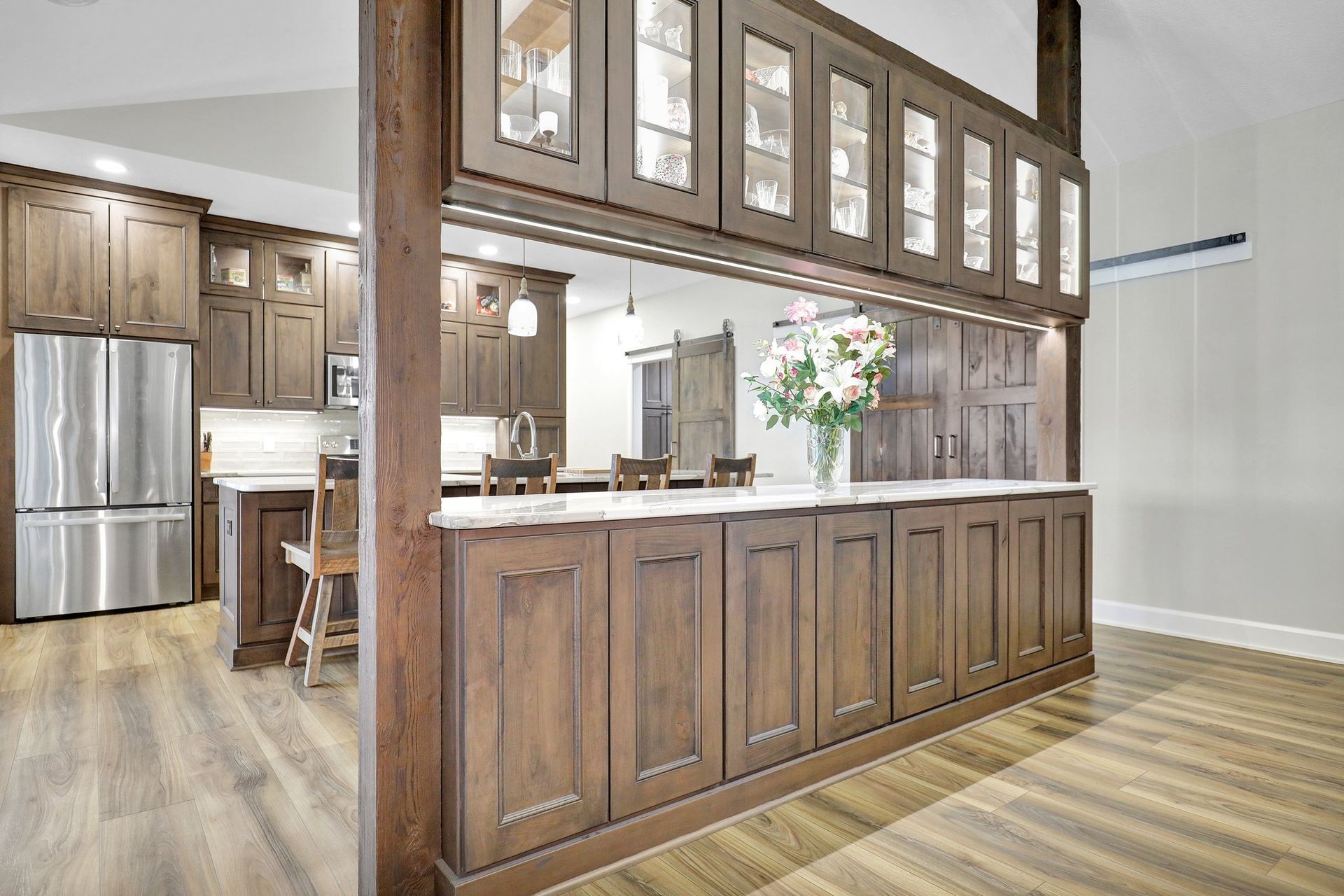 Open kitchen with wood cabinetry, stainless fridge, and breakfast bar with glass-front cabinets above.
