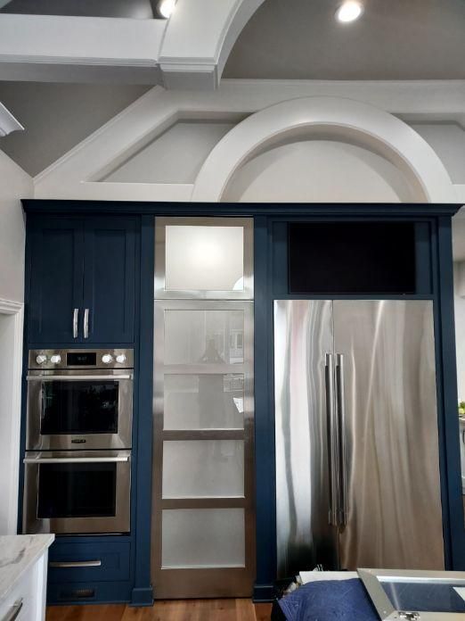 Modern kitchen with navy cabinets, stainless steel refrigerator, oven, and a frosted glass pantry door.
