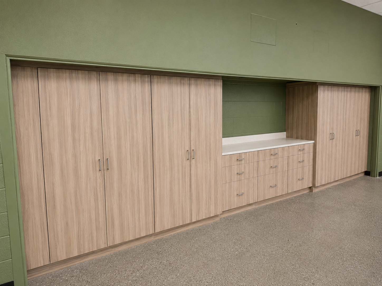 Built-in light wood cabinets with a countertop opening against a green wall in a room