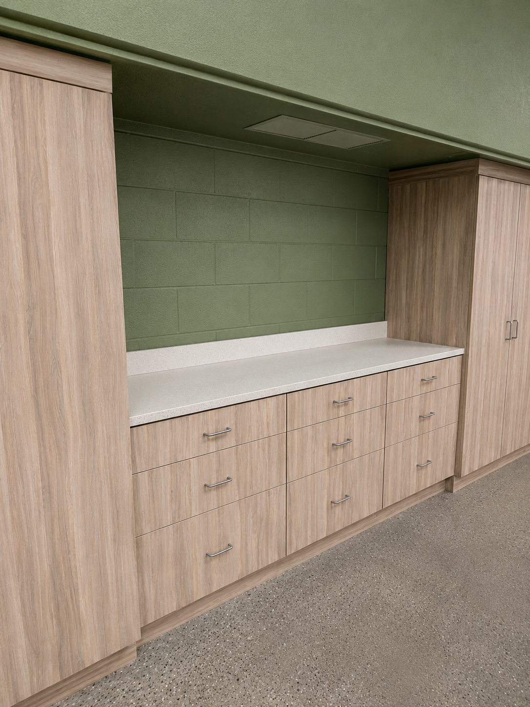 Built-in wooden cabinets with drawers and a white countertop beneath a green wall niche.