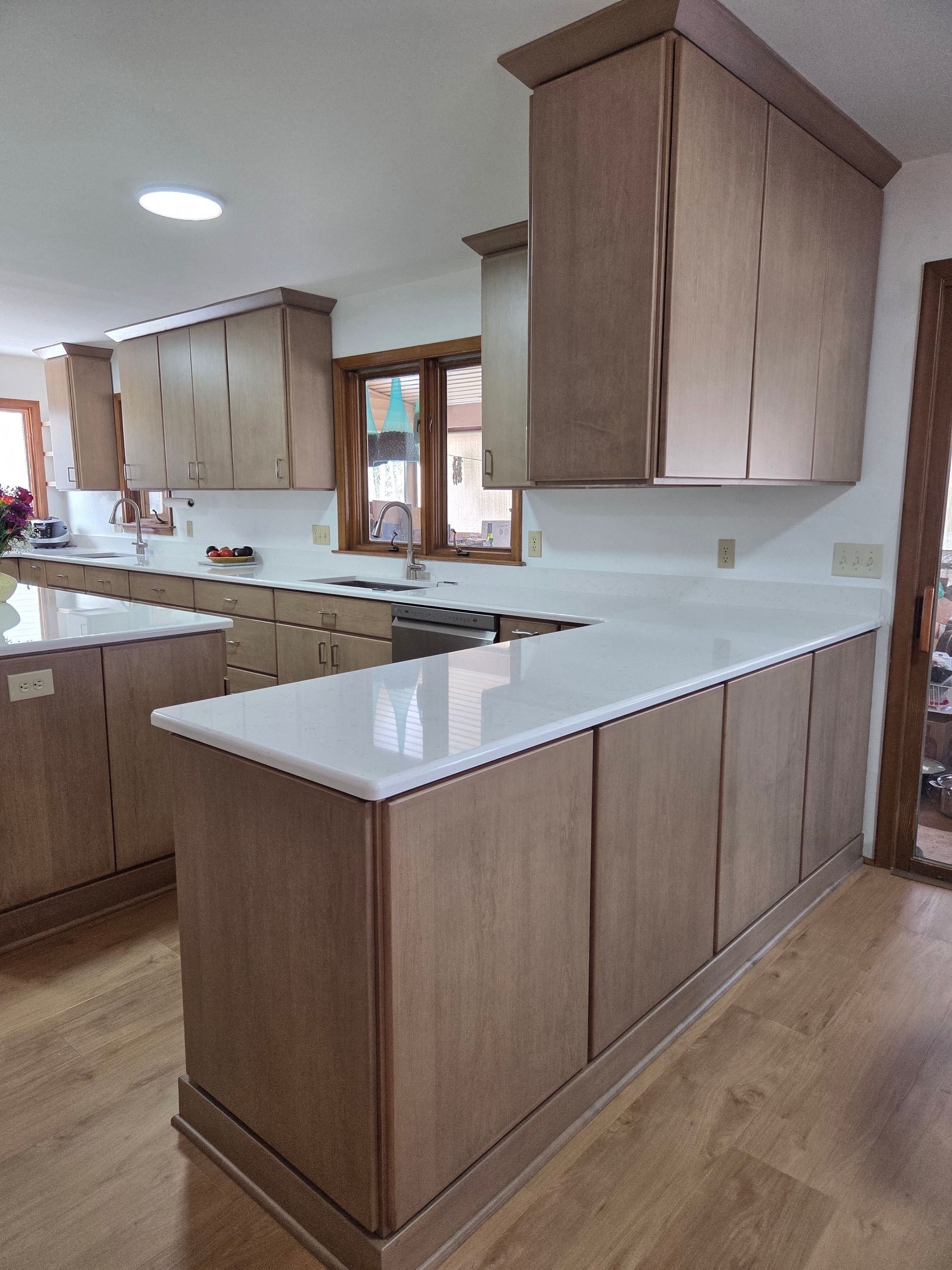 Modern kitchen with wood cabinets, white countertops, and a central island with a built-in cooktop.