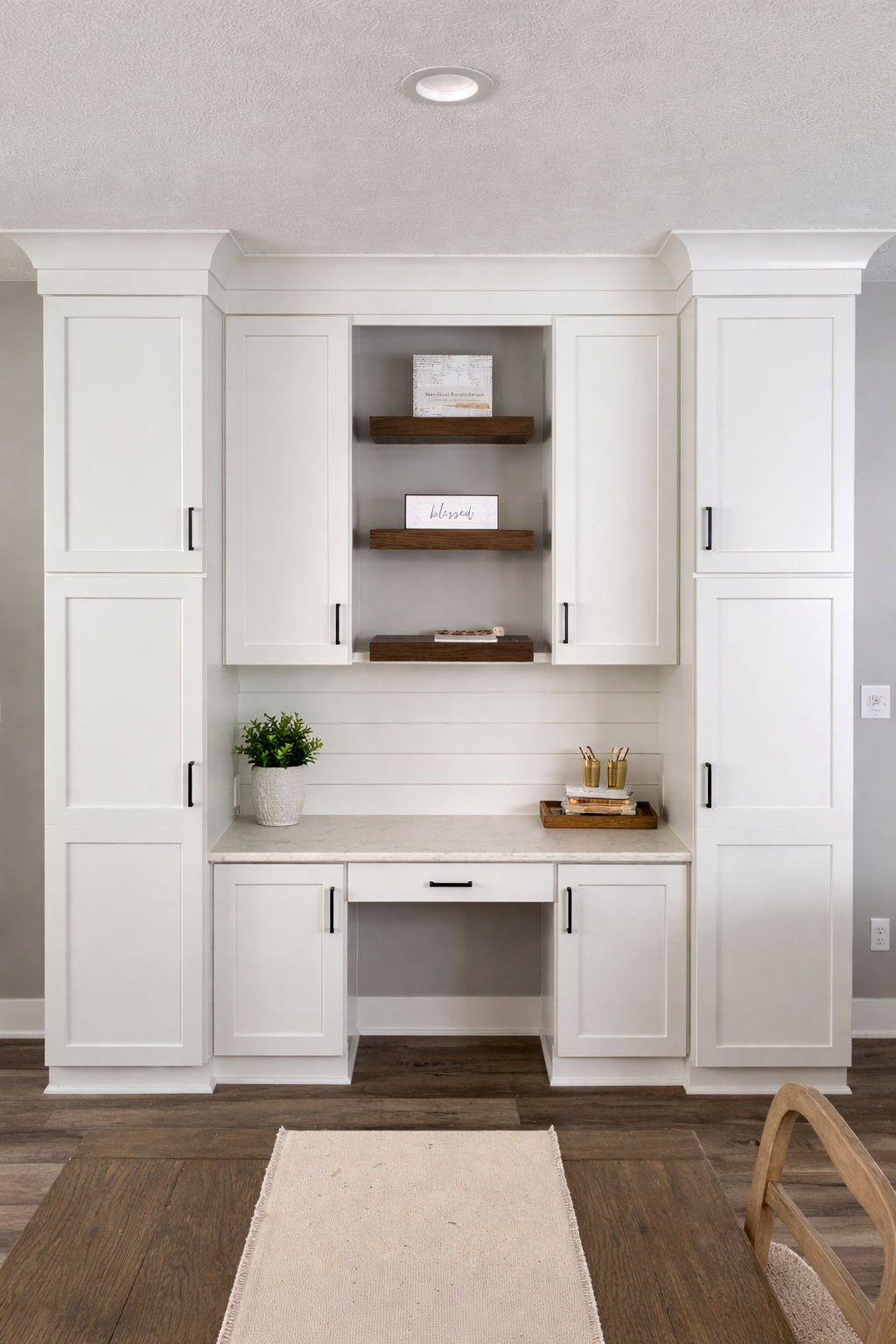 White built-in desk nook with cabinets, shelves, and a beige rug in a bright room