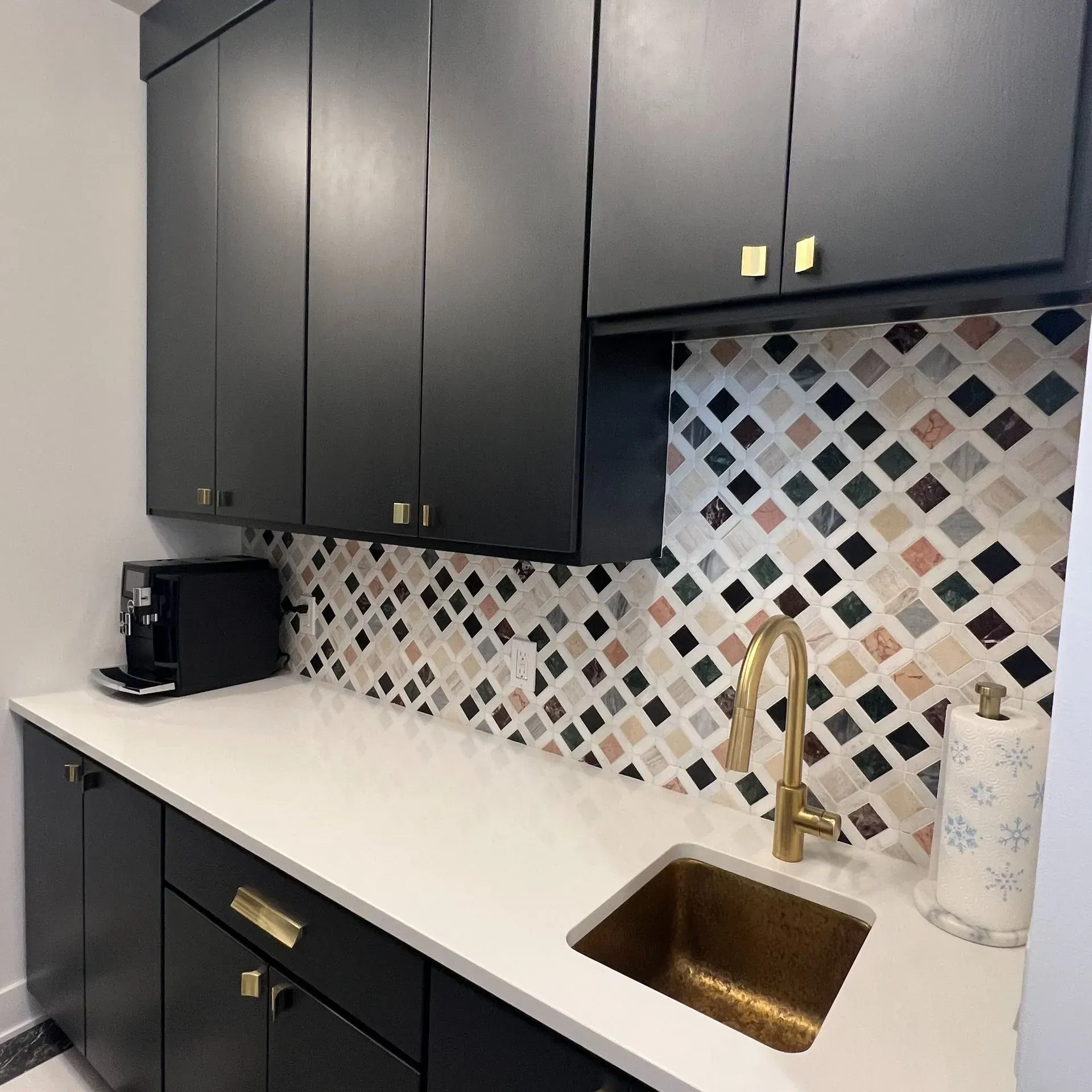 Modern kitchen with dark cabinets, white countertop, brass faucet, and colorful diamond-pattern tile backsplash