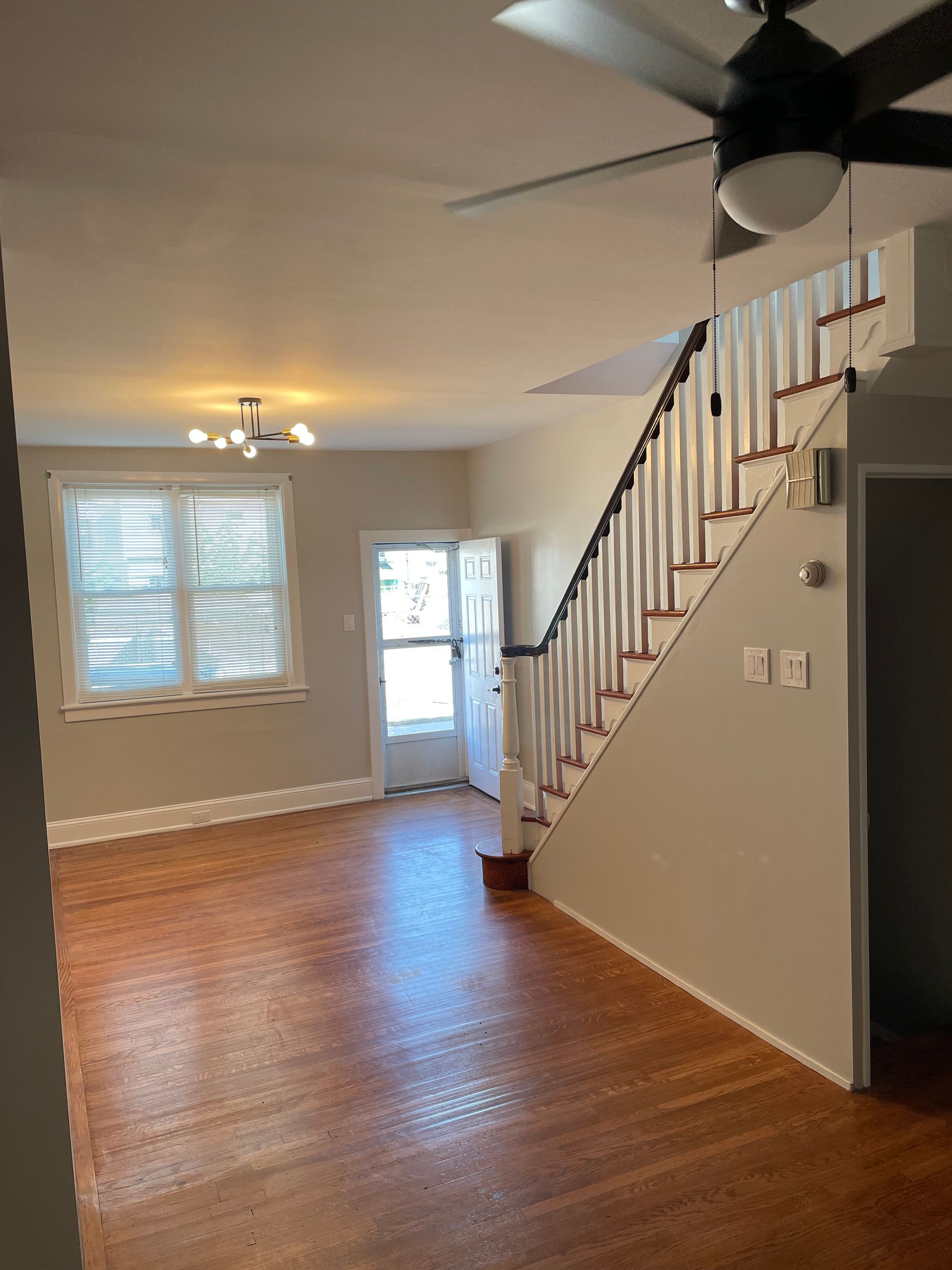 An empty living room with stairs and a ceiling fan