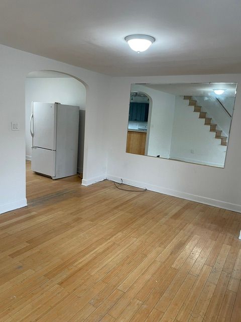 An empty living room with hardwood floors and a refrigerator.