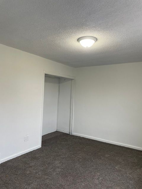 An empty bedroom with white walls and a brown carpet.