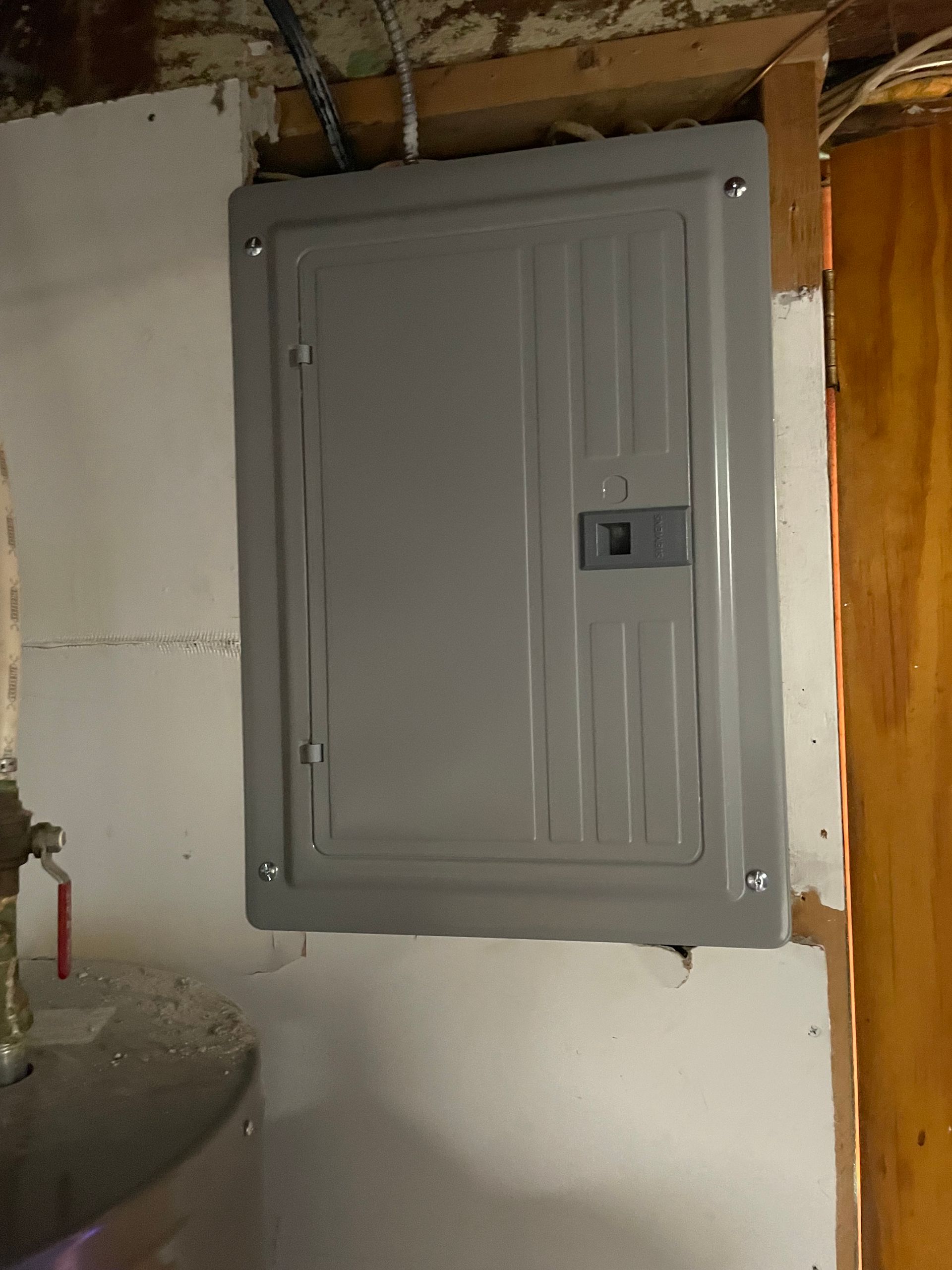 A gray electrical box is hanging on a white wall next to a wooden door.