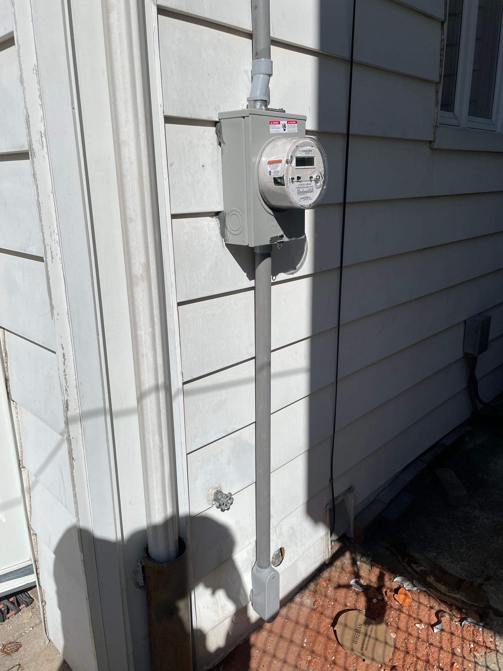 A gas meter is sitting on the side of a white house.